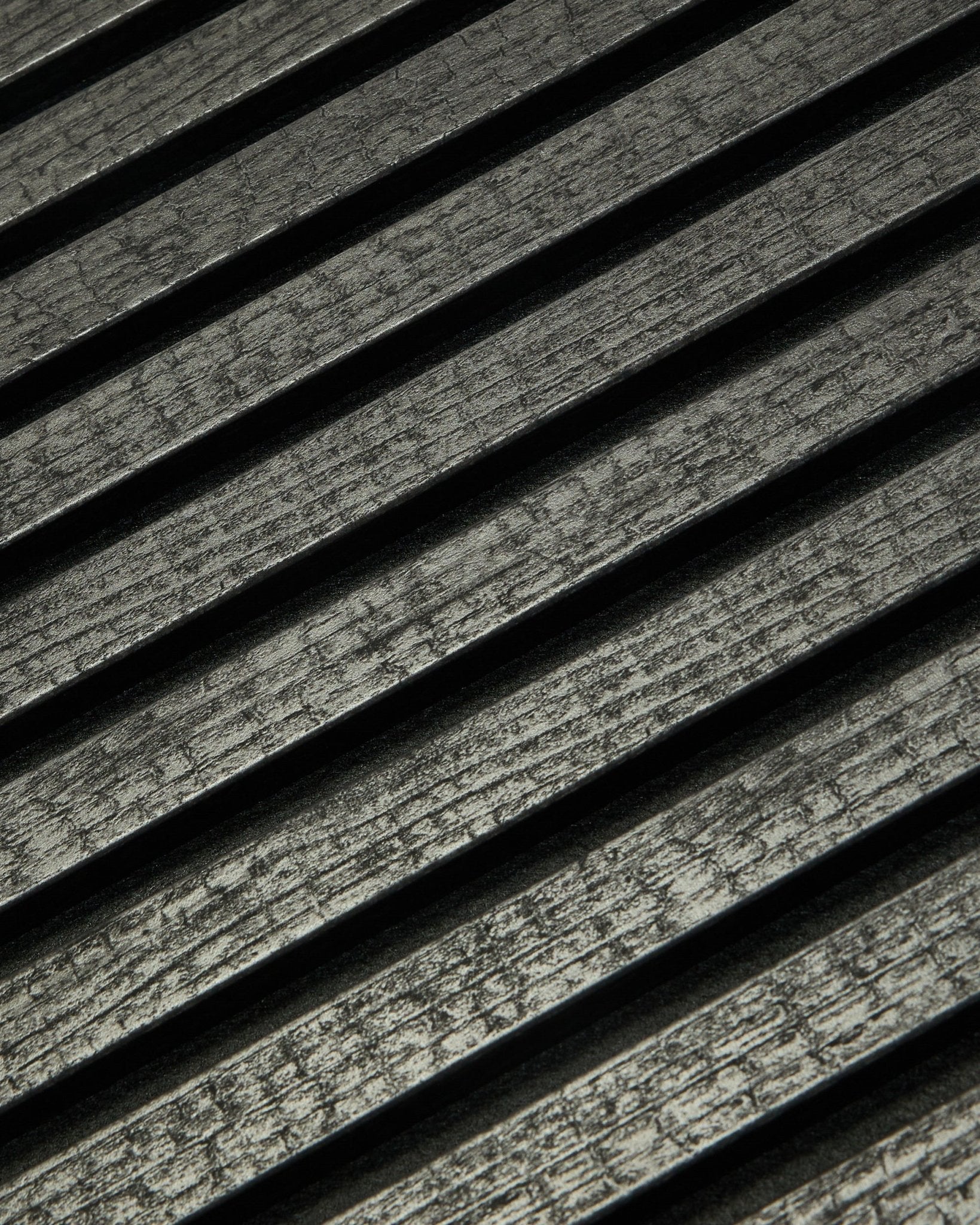 Nahaufnahme des WoodUpp Rebel Akupanel in Charcoal (240x60 cm), die black, gerillte Akustiklamellen zeigt, die diagonal angeordnet sind, um die Schallabsorption zu verbessern.