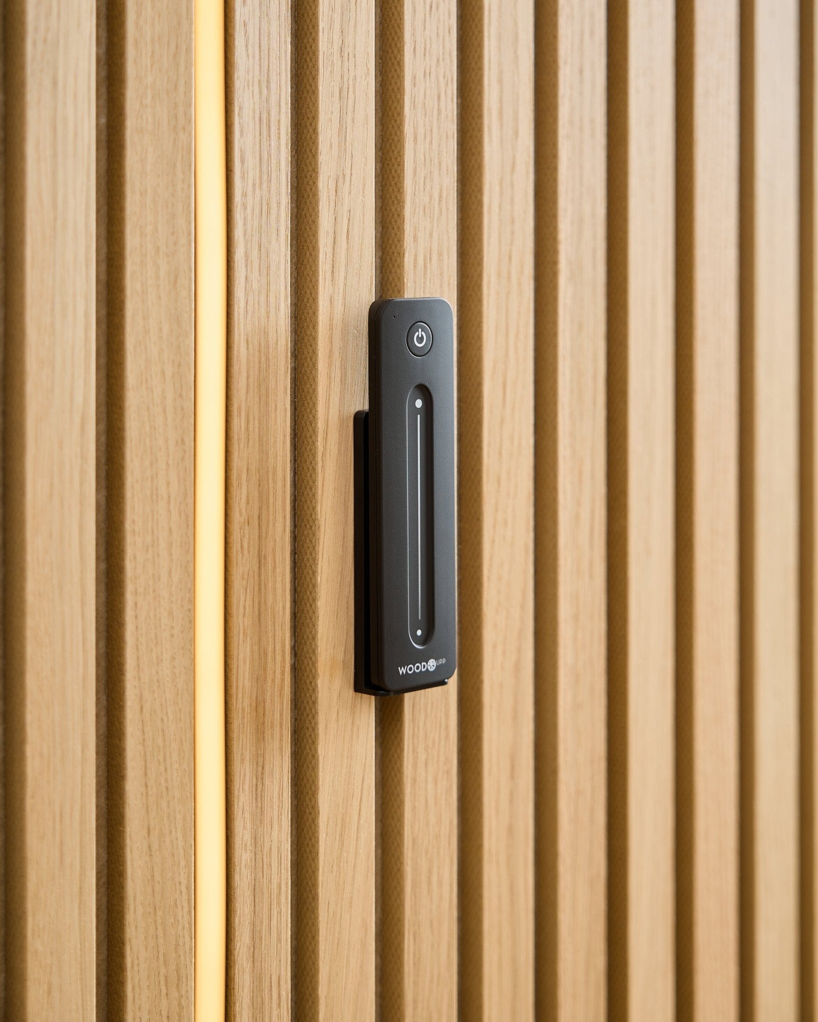 Ein WoodUpp Lumi | Remote / LED Striplight ist auf einer hellen Holz-Akustikpaneel installiert, mit einem gelben Kabel, das hinter den Holzlamellen sichtbar ist.
