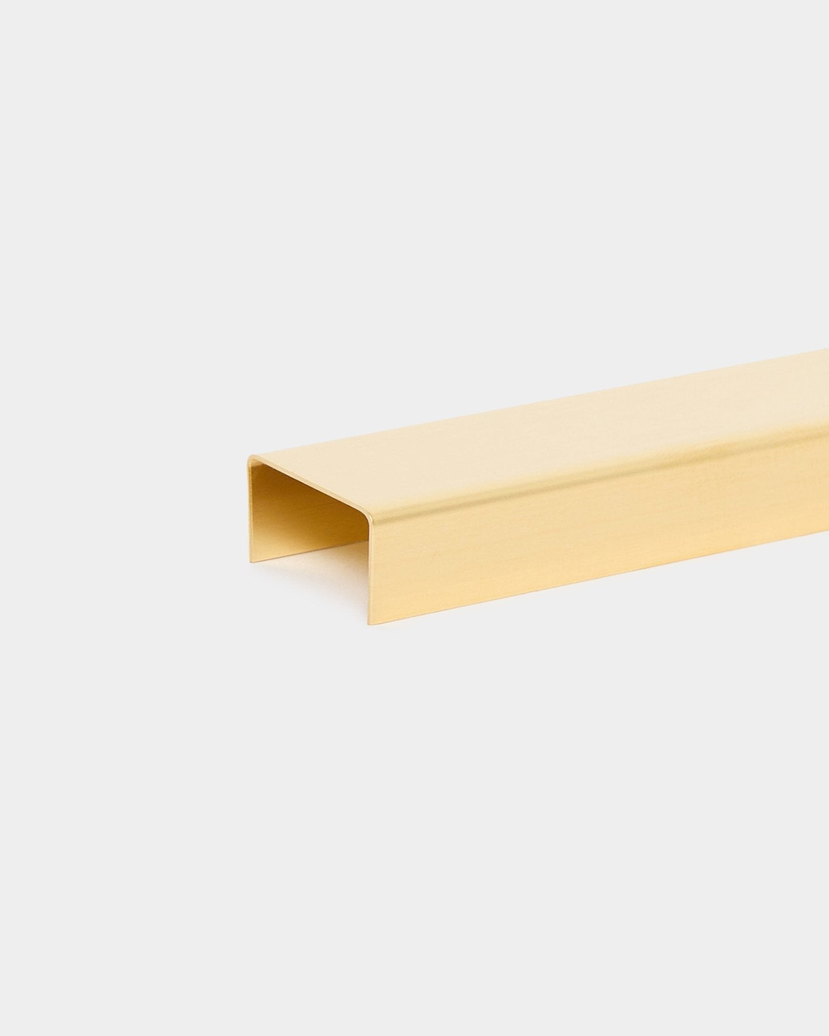 Die Liva | Cover in brass, 60 cm von WoodUpp ist ein U-förmiges Metallleisten-Zubehör für Akupanel Akustikpaneele, dargestellt vor einem schlichten hellgrauen Hintergrund.