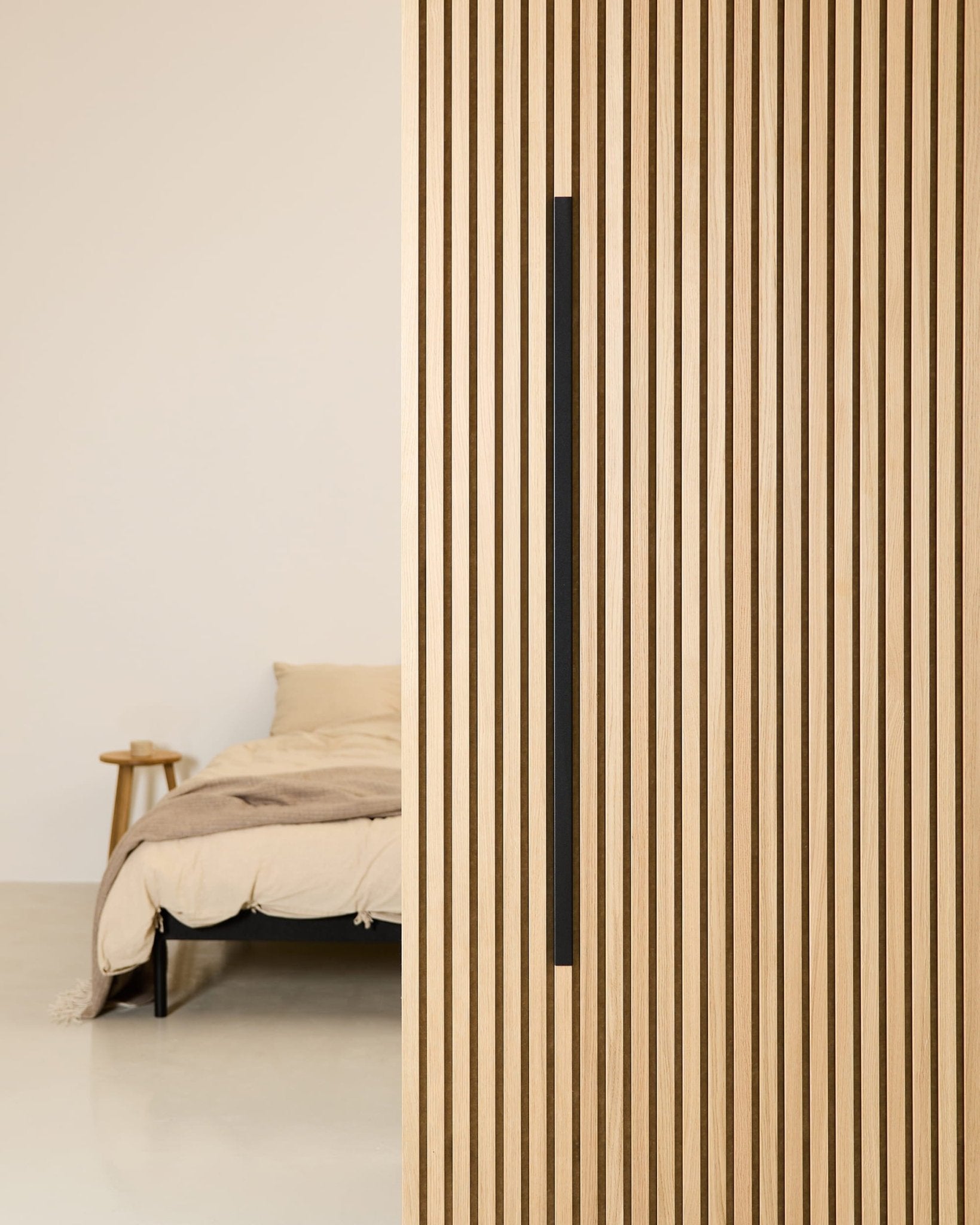 Minimalistisches Schlafzimmer mit einem beigen Bett, einem Beistelltisch aus Holz und einer an der Wand montierten Akustikplatte WoodUpp Akupanel Black Aluminum 120 cm.