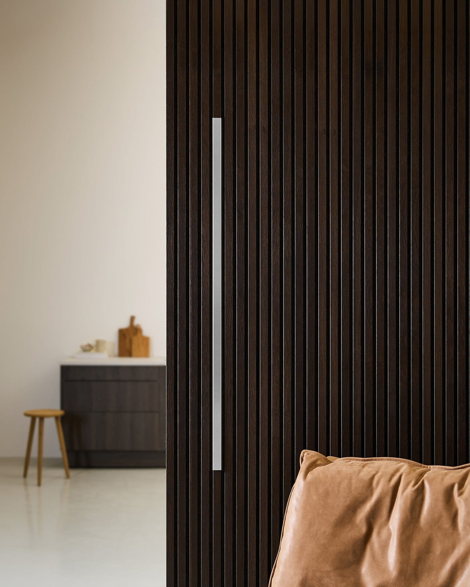 Akupanel-Tür aus dunklem Holz mit WoodUpp Liva Cover, 120 cm langem Stahlgriff, Zierleiste, Lederpolster und minimalistische nordische Küche mit Hocker.