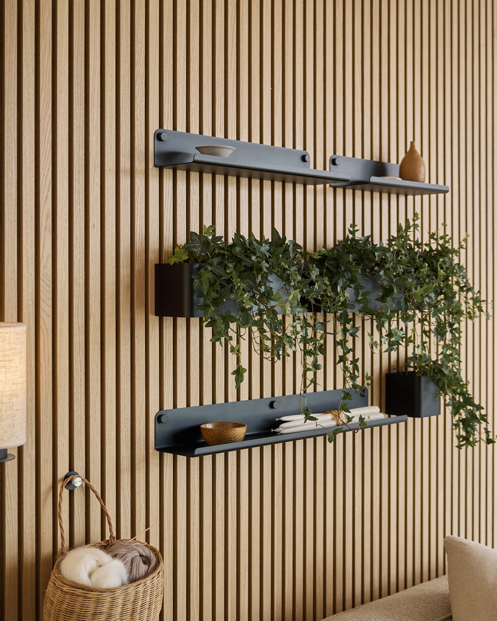 Drei black Norr | Plant Box Regalböden von WoodUpp mit Deko und einer Pflanze sind über einem Weidenkorb mit Garn montiert, vor einem grünen Akustik-Lamellenpaneel.