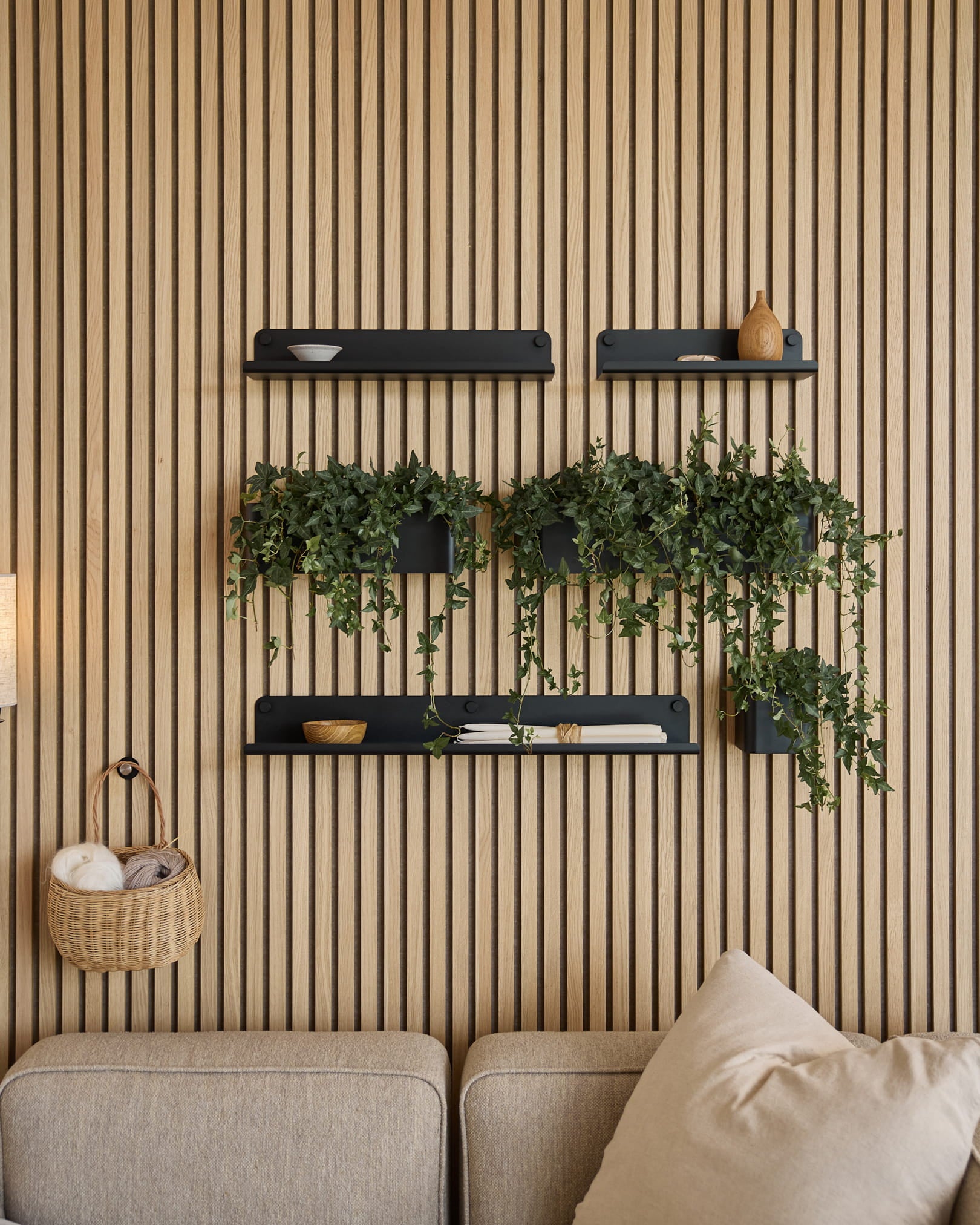 Modernes Wohnzimmer mit nordischem Akustik-Lamellenwandpaneel, black Regalböden, hängenden Pflanzen in WoodUpps Norr Plant Box (35,9 cm, Black) und einem beige Sofa.