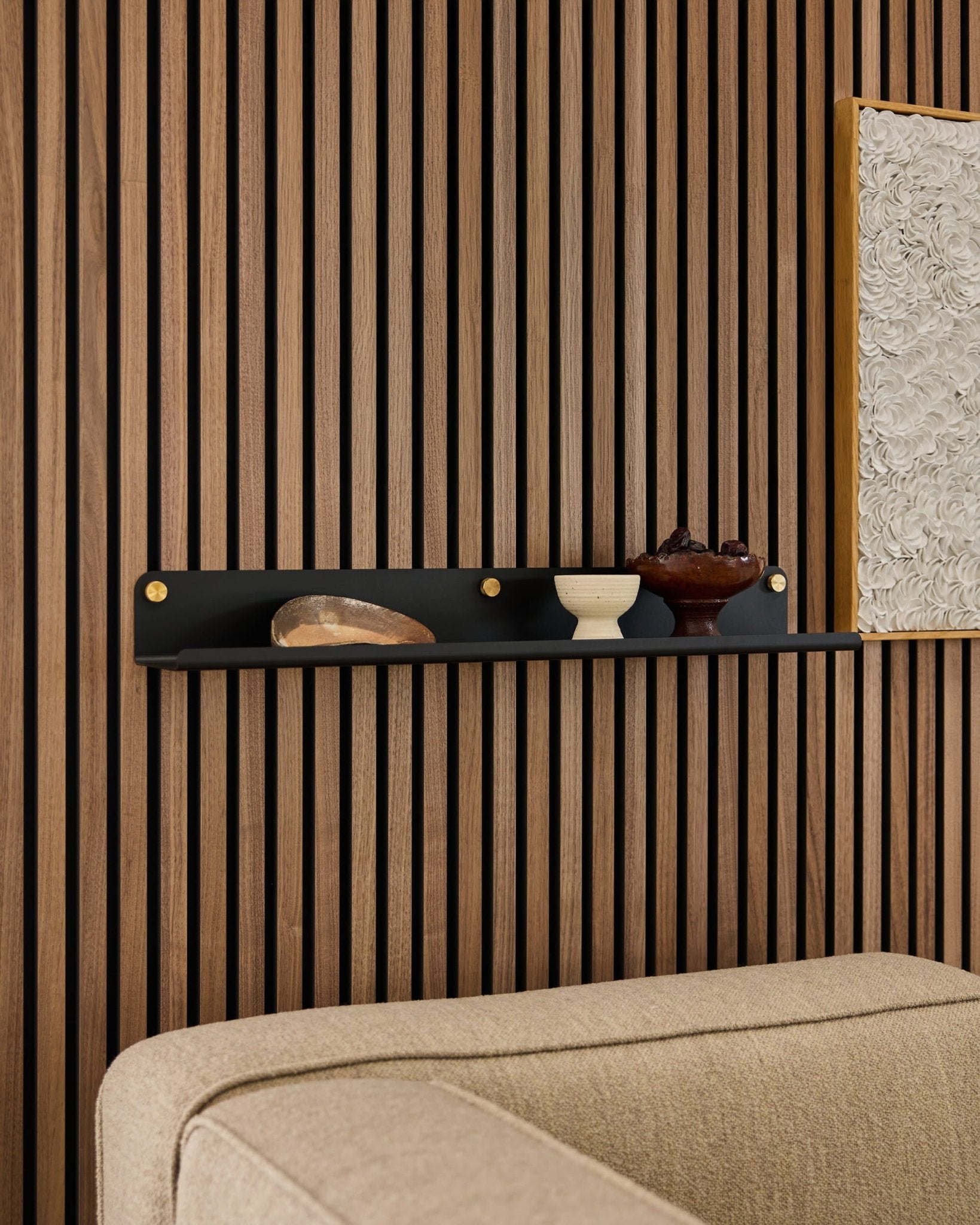 Breites Regal WoodUpp Norr in Schwarz (75,9 cm) mit Dekor über einem beigen Sofa, montiert an einer modernen Akustik-Lamellenwand aus Holz.