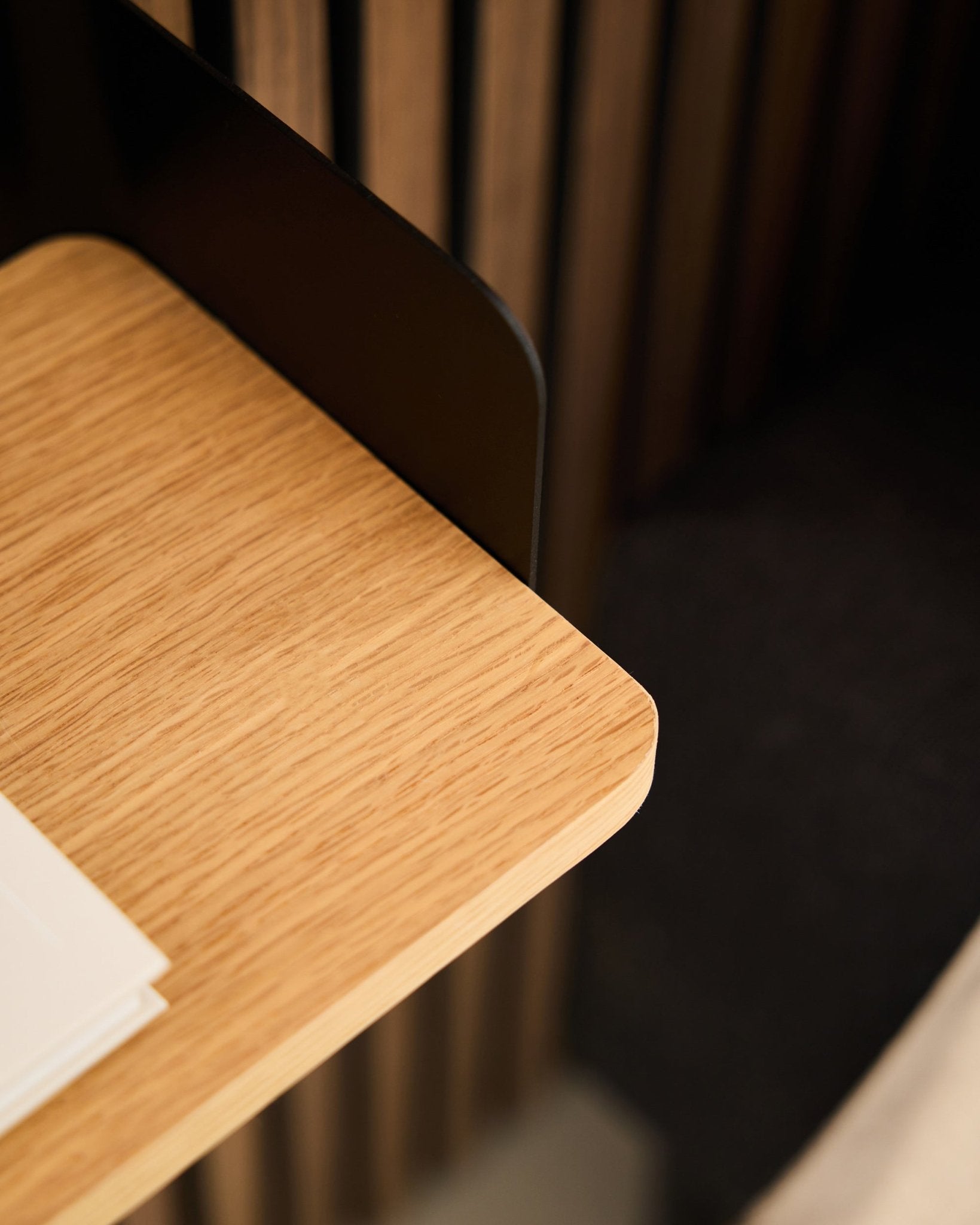 Nahaufnahme einer Schreibtischecke mit Akustikholzpaneelen in black Akupanel, weißen Papieren und dem WoodUpp Linn Bücherregal in Natural Oak (39,9 cm) im Hintergrund.