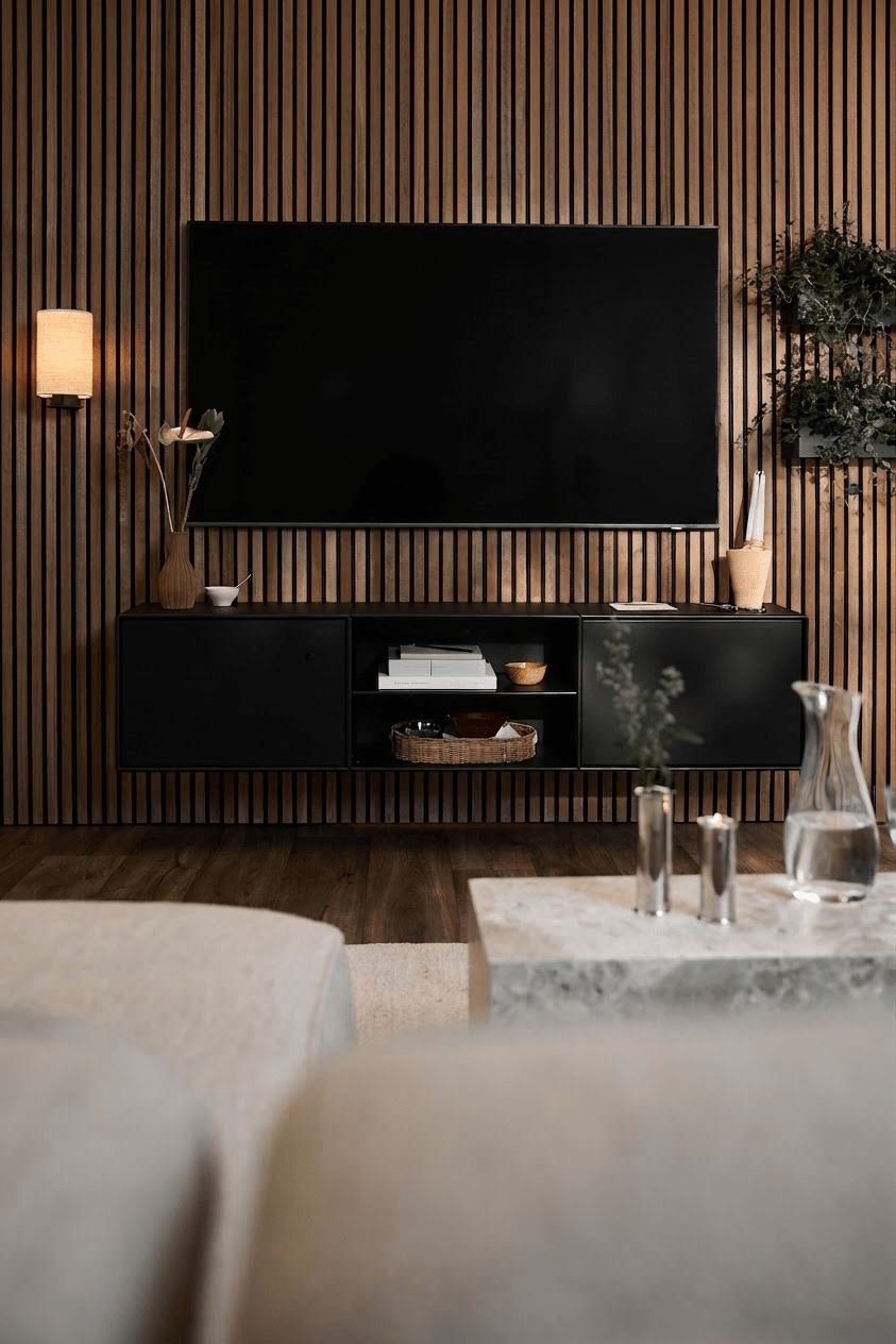 Modernes Wohnzimmer mit dem TV-Schrank „WoodUpp Arka“ in Schwarz, einer Akupanel-Lamellenwand, minimalistischen Akzenten und einem hellen Sofa mit Couchtisch.