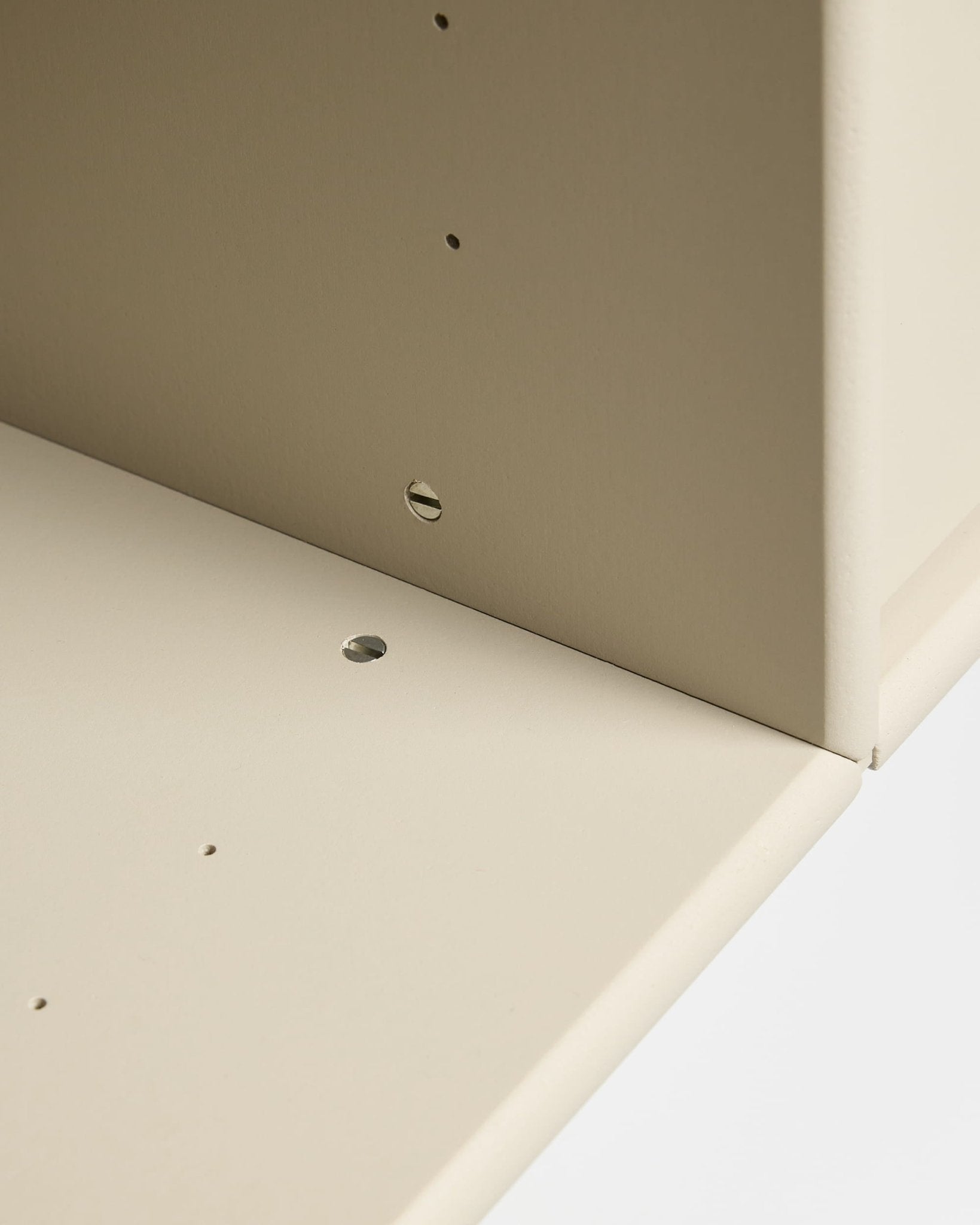 Nahaufnahme von zwei beigen Arka-TV-Konsole-Platten von WoodUpp, die im rechten Winkel miteinander verbunden sind und über vorgebohrte Löcher für den modularen Zusammenbau und die Kabelführung verfügen.