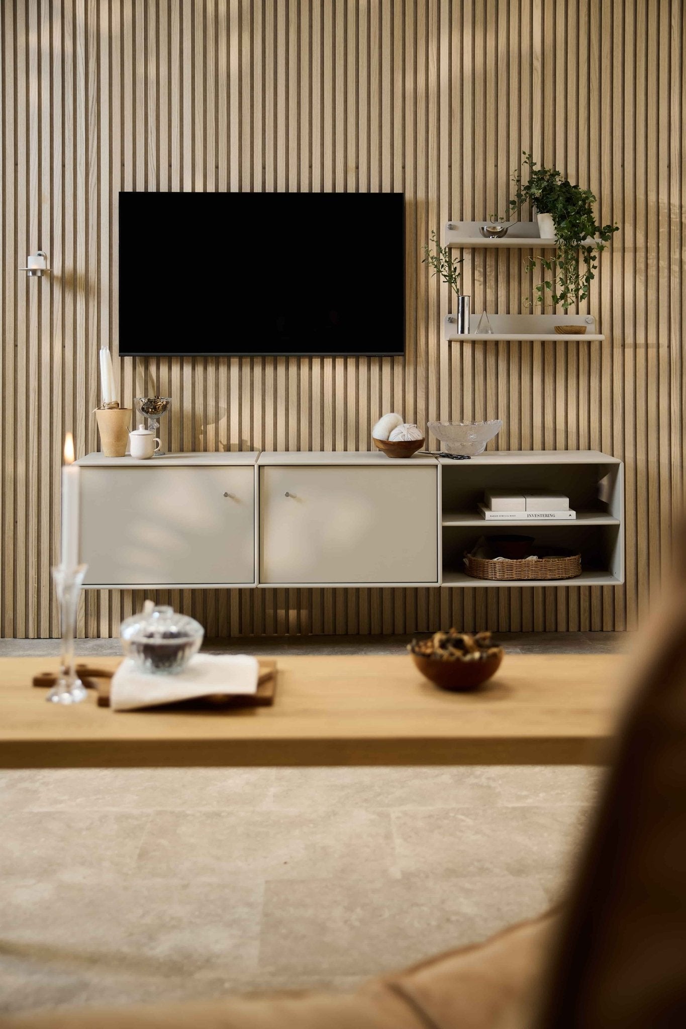 Modernes Wohnzimmer mit dem TV-Möbel „Arka“ von WoodUpp, modularen Sitzmöbeln, Regalen im nordischen Stil mit Pflanzen und Deko sowie einer Kerze auf dem Couchtisch.