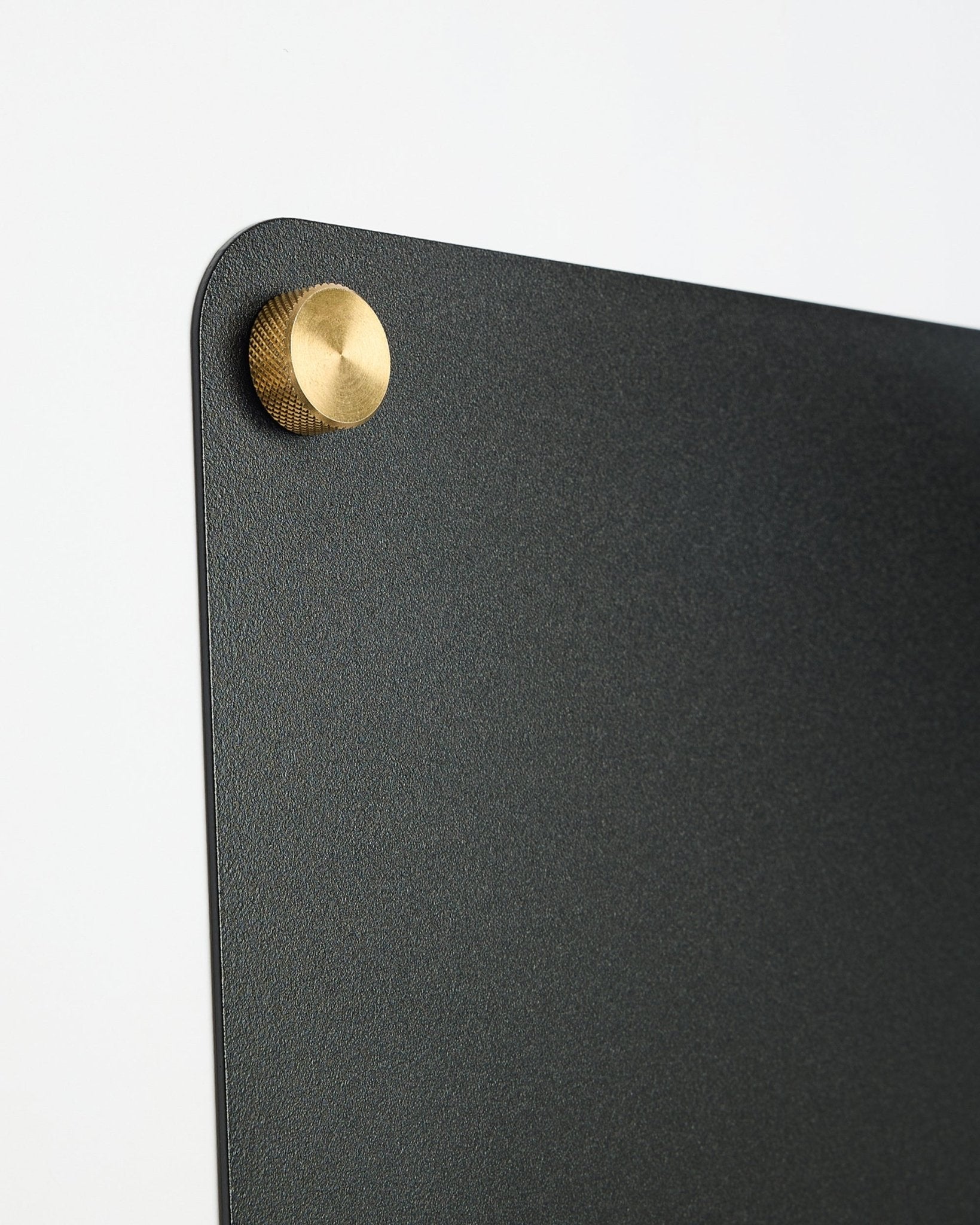 Nahaufnahme einer large black Norr Magnettafel von WoodUpp aus der CREATE-Kollektion mit einem runden Metallverschluss in Gold-colored in der oberen Ecke.