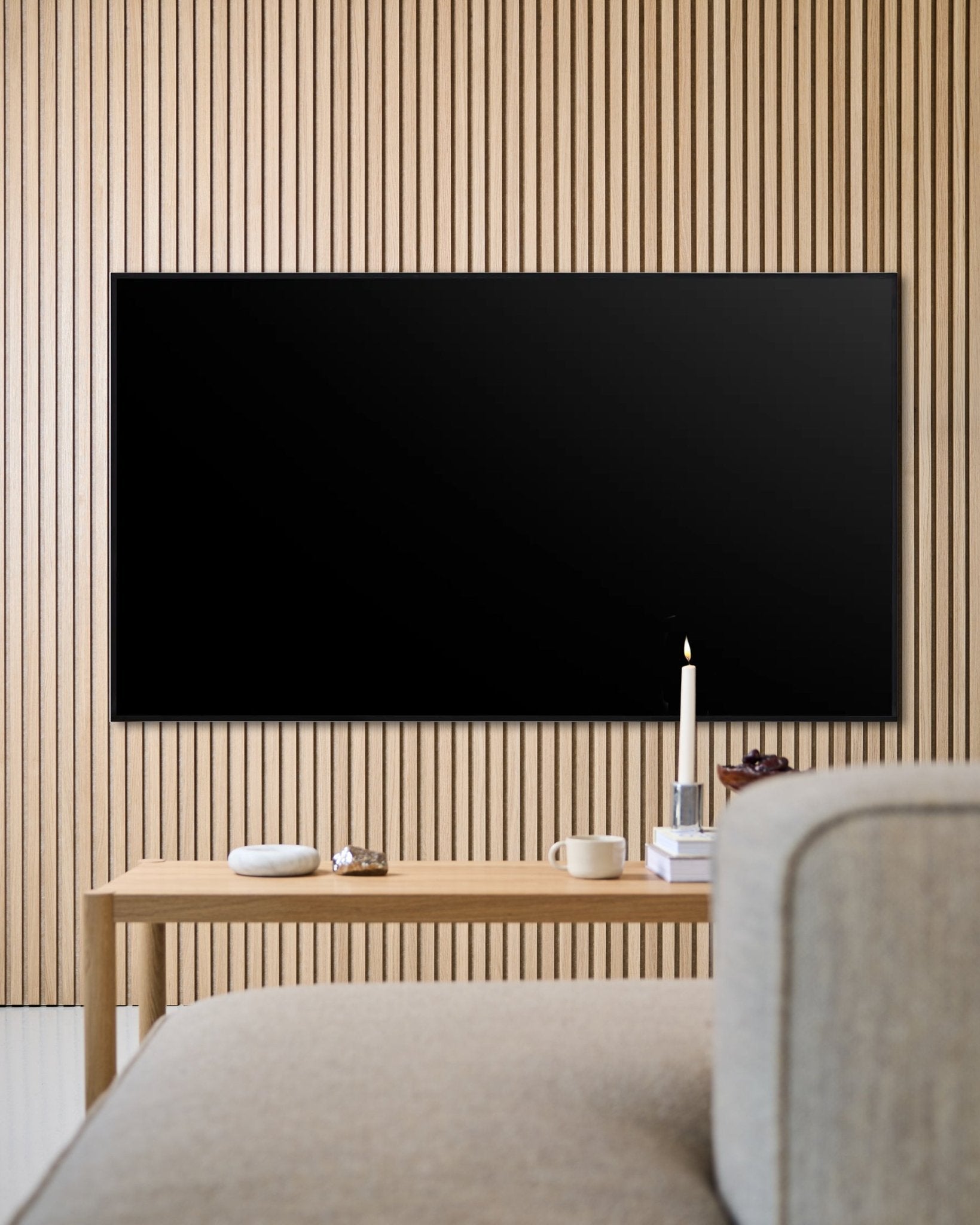 Modernes Wohnzimmer mit einem wandmontierten Flachbildfernseher, Akupanel Akustikpaneelwand aus Holzlamellen und einem Couchtisch aus Holz für eine wohnliche Atmosphäre.