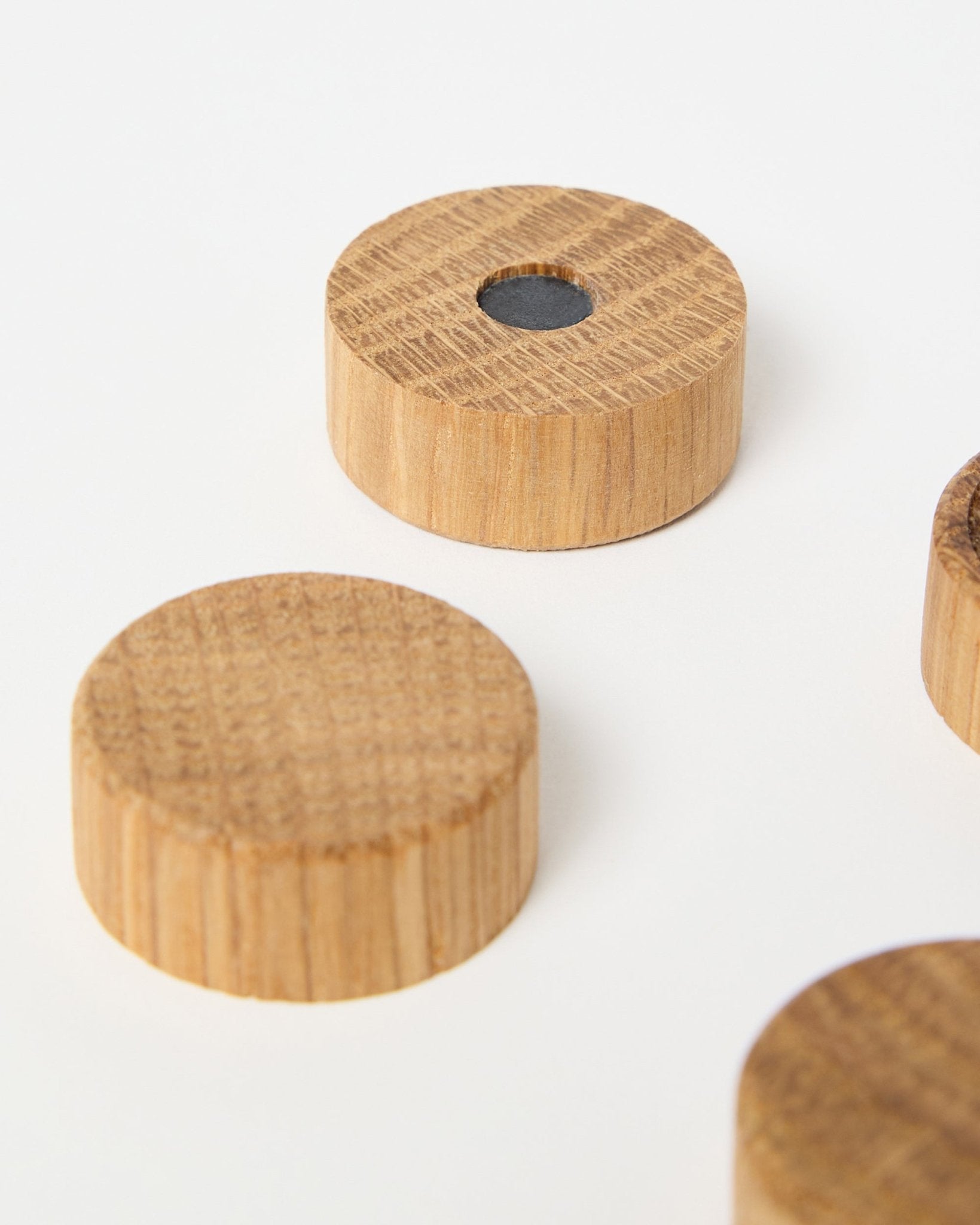 Set mit vier natural oak Magneten von WoodUpp, entwickelt für die Verwendung mit Akupanel Akustikholzpaneelen, einer davon mit zentralem Neodym-Magneten für extra Halt, auf Weiß präsentiert.