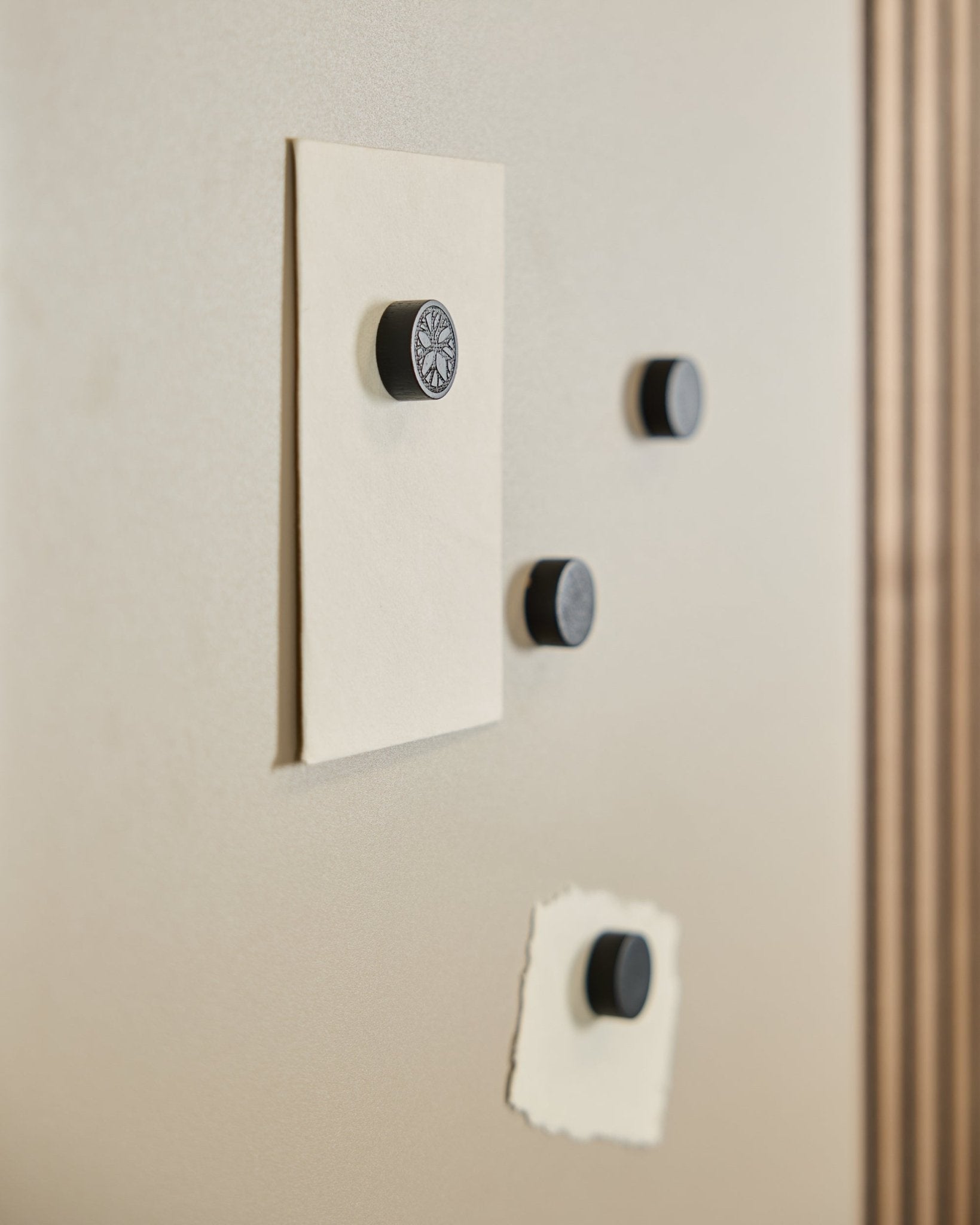 Vier WoodUpp Norr Magnet-Set in Black Oak (4 Stk.) befestigen zwei Blätter auf einem Norr Magnetic Board, rechts ist ein Teil eines Akustikpaneel sichtbar.