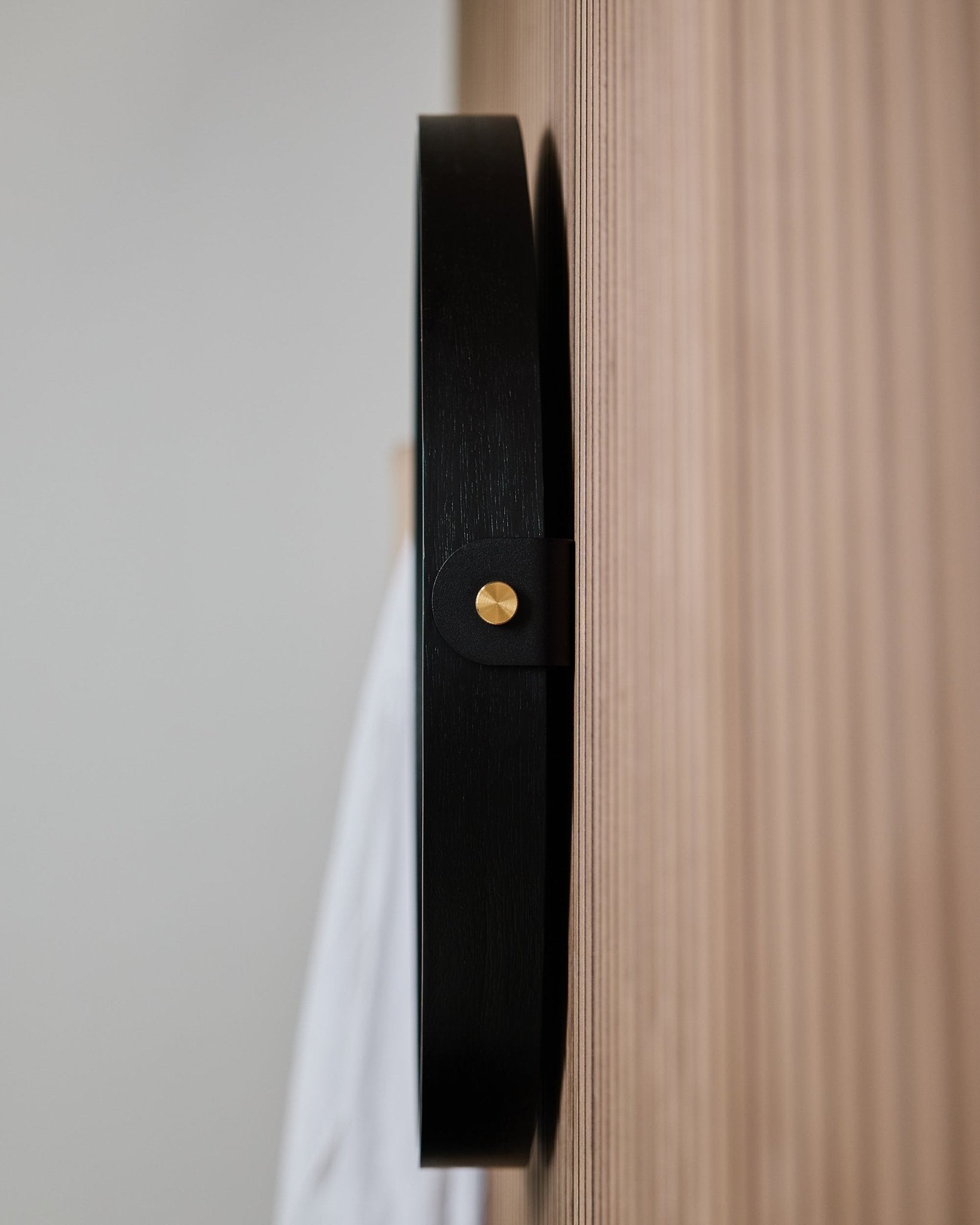 Nahaufnahme der Seitenansicht des WoodUpp Linn | Mirror / Black Oak Wandhakens, montiert auf einer gerillten Eichen-Akustikpaneel, gestaltet zum Aufhängen eines runden Spiegels.