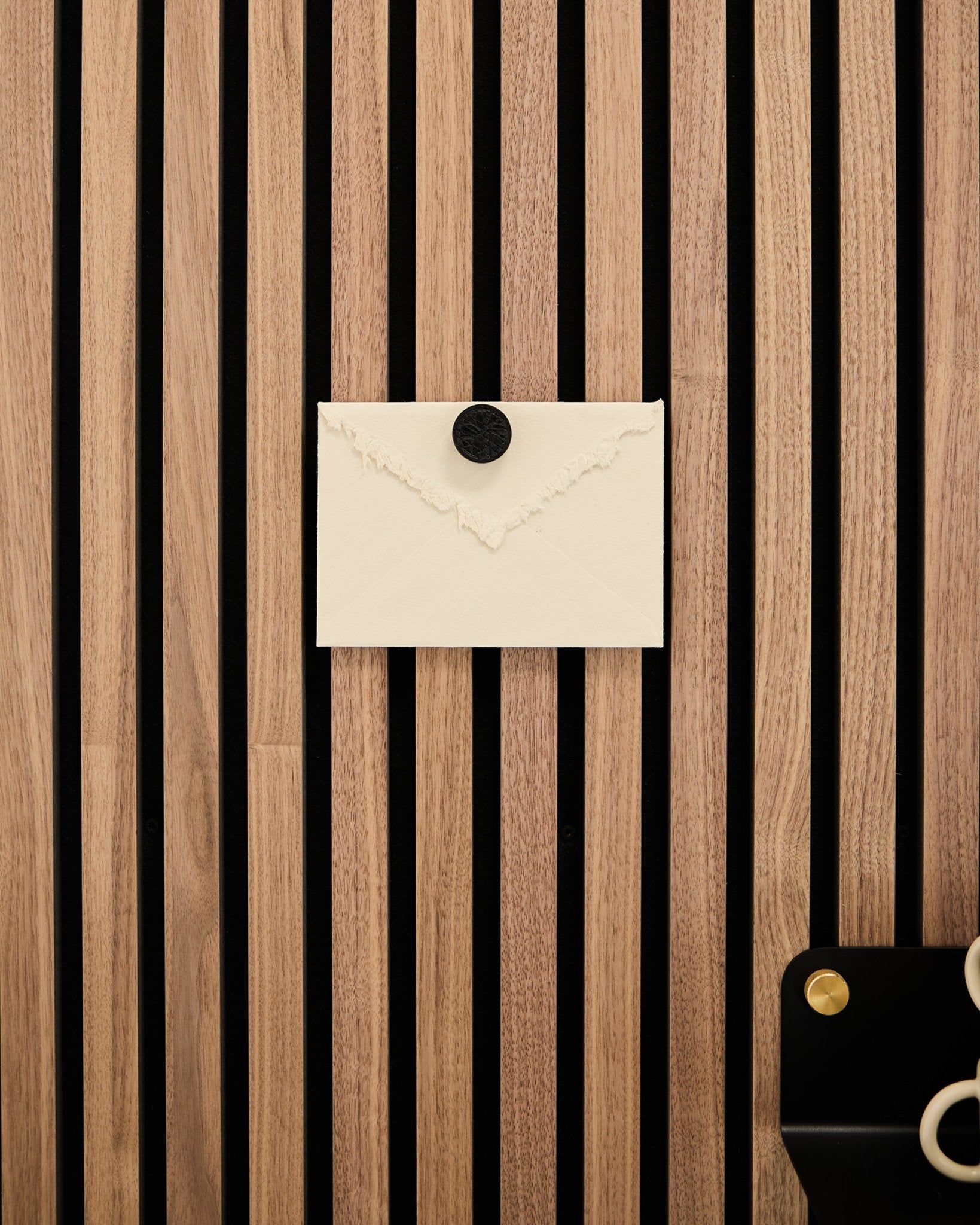 Ein cremefarbener Umschlag ist mit dem Norr Poster Magnet-Set in Black Oak an einem WoodUpp Akupanel Eichen-Akustikpaneel mit Akustikpaneel befestigt; unten rechts liegt eine Schere.