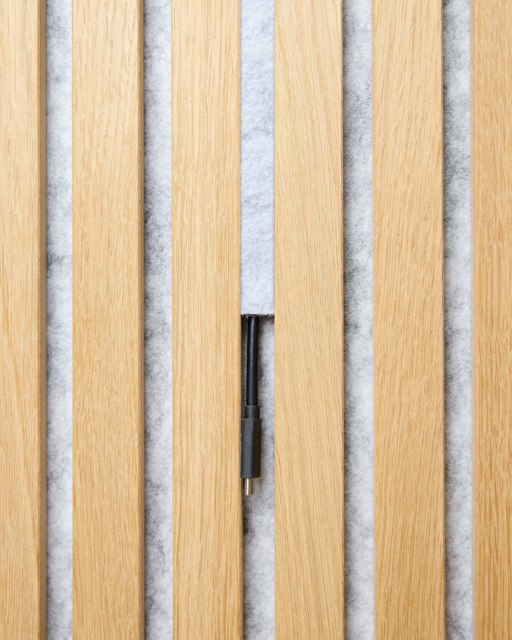 Das Dupps Pop-on Cable Cover Set (grey, 3 Stk.) von WoodUpp ordnet Kabel zwischen hellen Holz-Akupanel auf einem weißen, strukturierten Hintergrund.