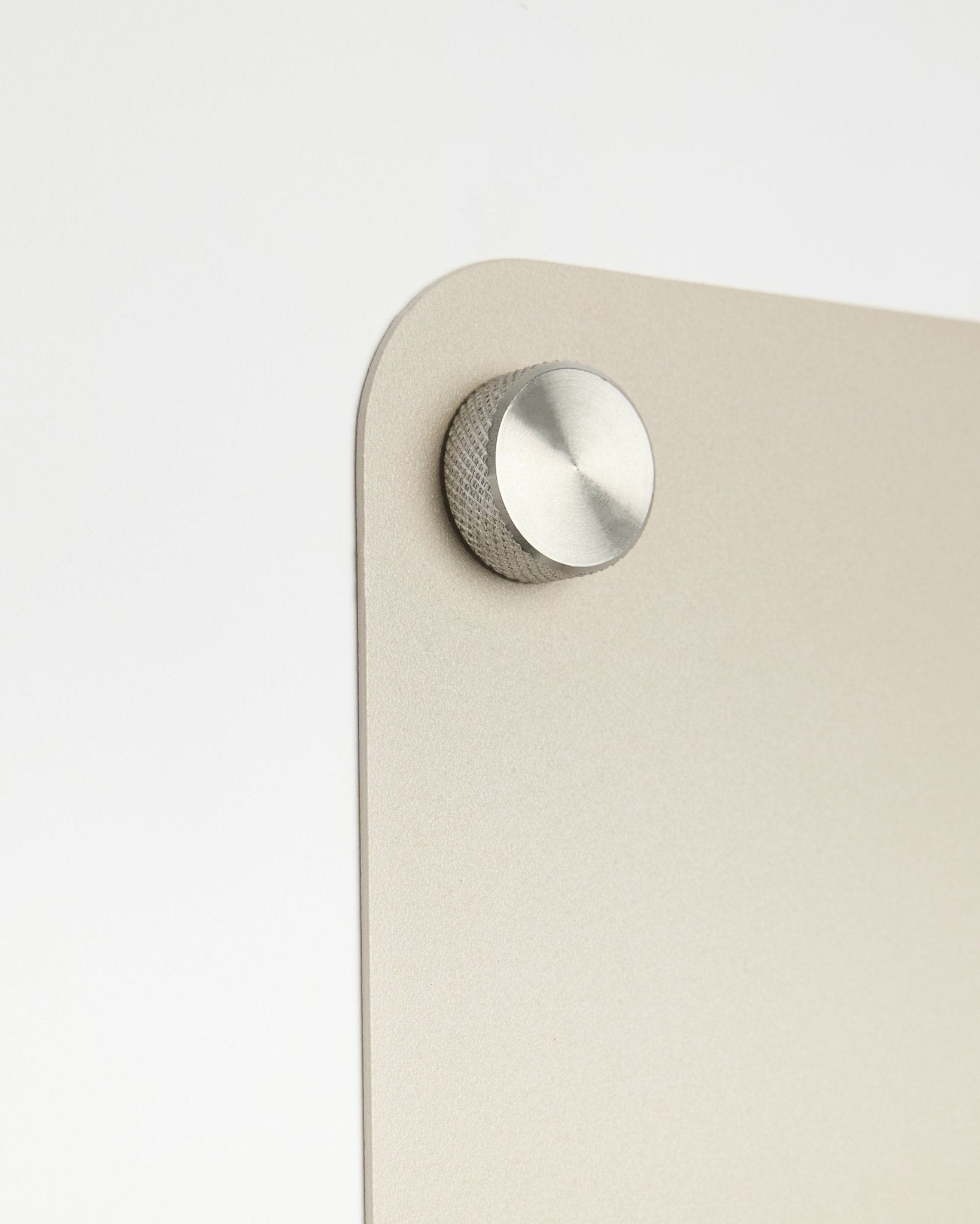 Nahaufnahme eines runden Metallknaufs als Zubehör, befestigt an der large beige Norr Magnettafel von WoodUpp, mit Detail aus satiniertem Glas vor weißem Hintergrund.