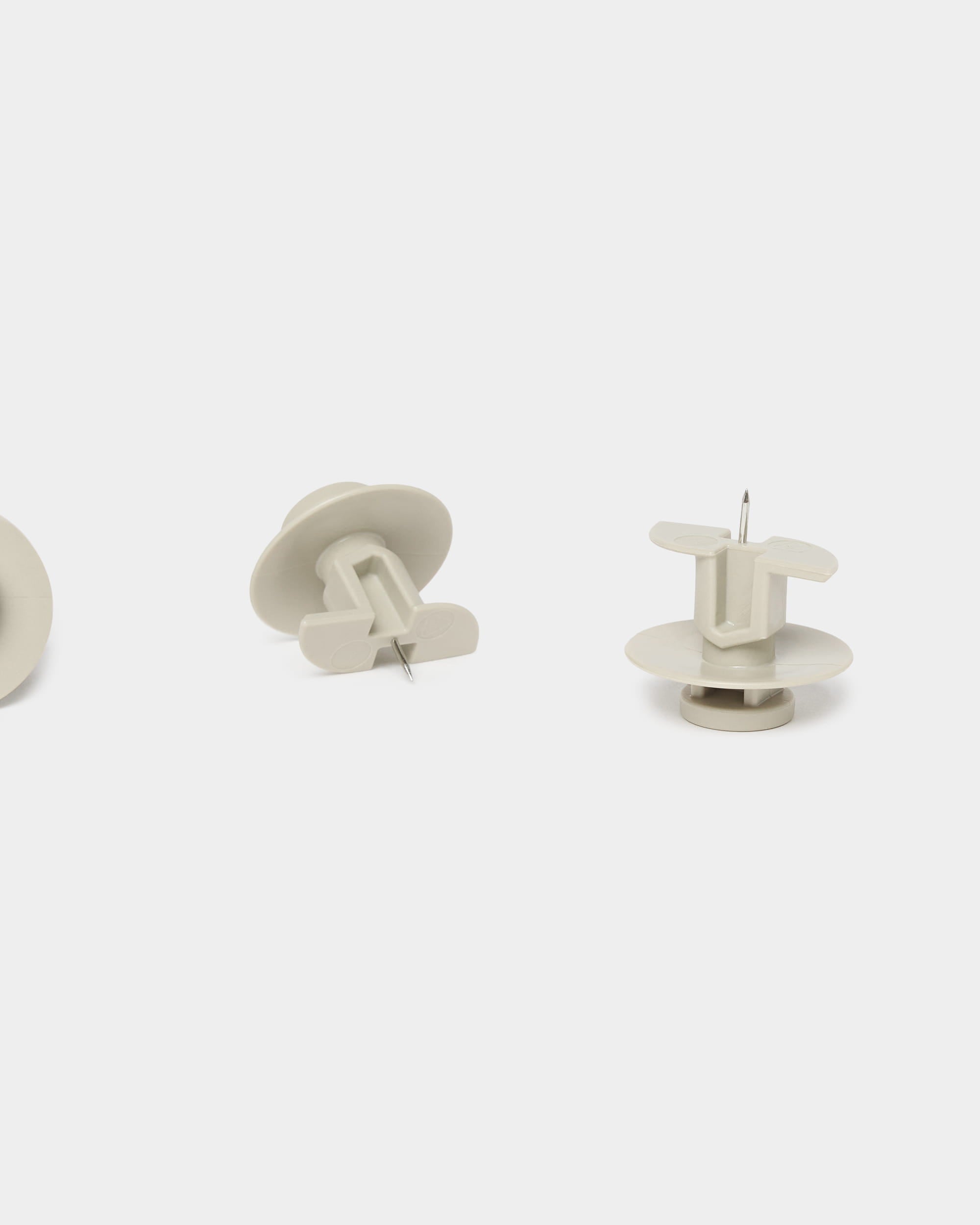 Set aus drei beigen WoodUpp Dupps-Reißnägeln und einem Werkzeug, entwickelt für Akupanel-Akustikplatten, dargestellt in aufrechter und seitlicher Position vor einem schlichten weißen Hintergrund.