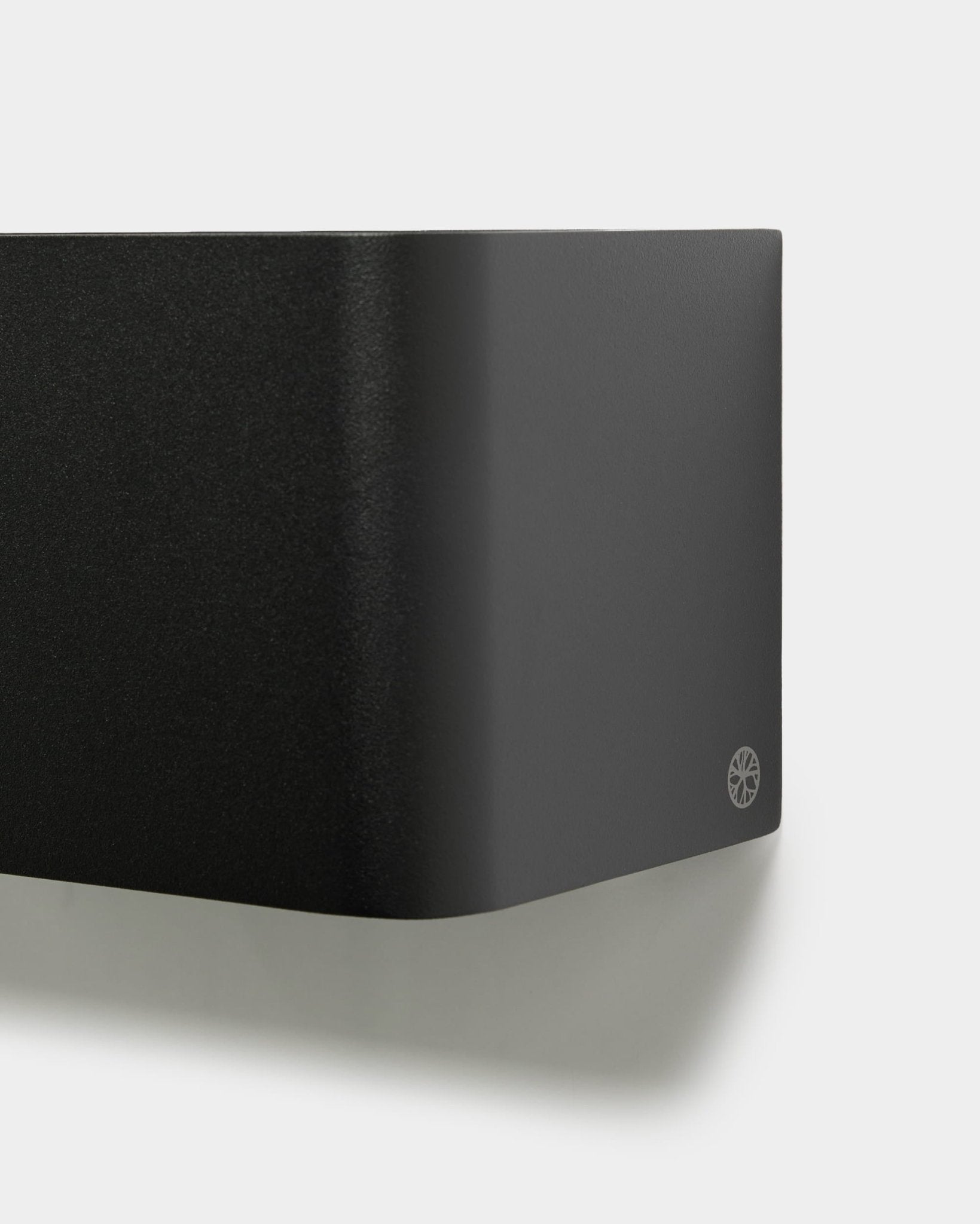 Nahaufnahme der minimalistischen WoodUpp Norr Pflanzbox (23,9 cm, black) mit abgerundeten Kanten und Logo, an einer weißen Wand montiert. Nordisches Akustik-Accessoire-Design.