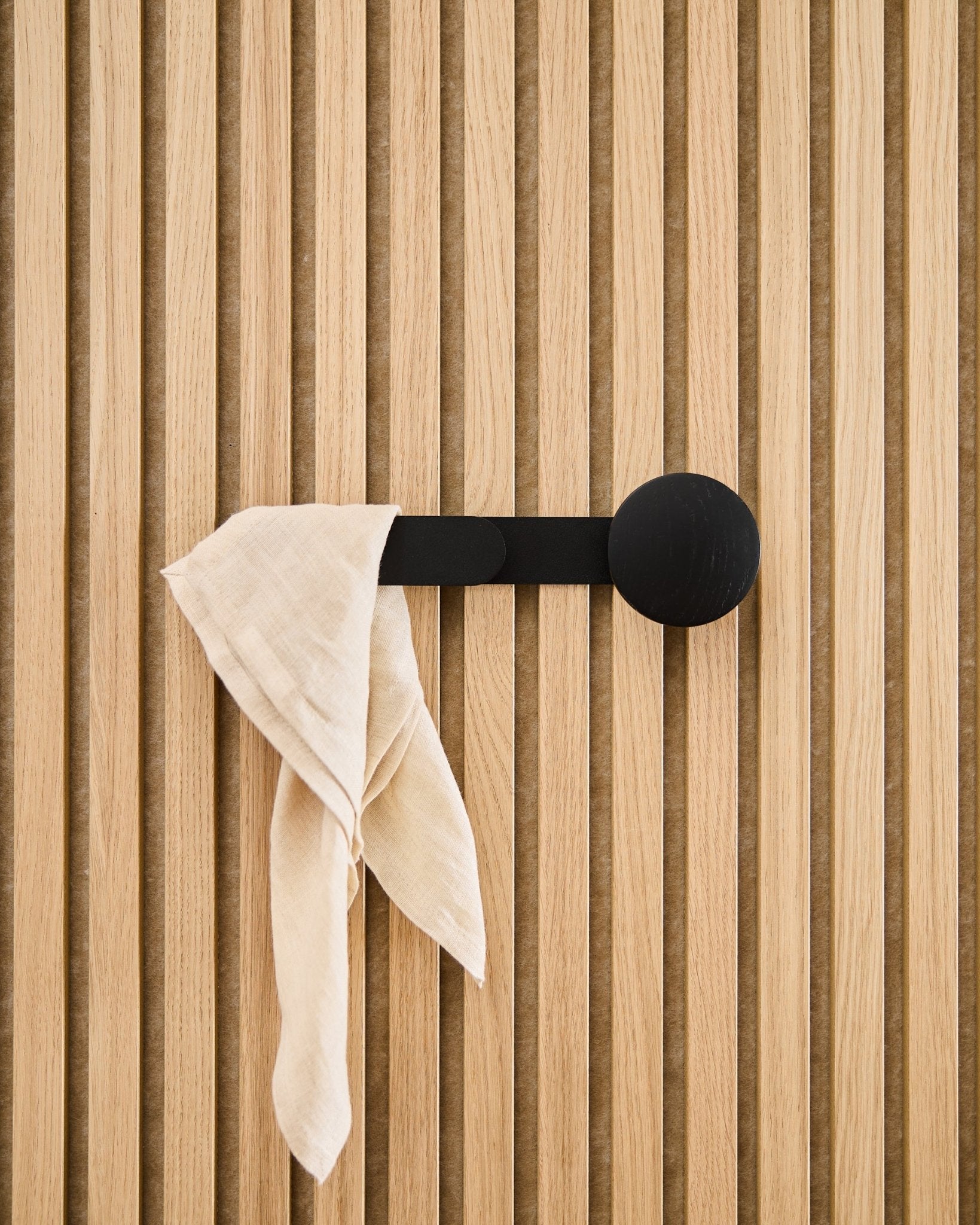 Ein beige Tuch hängt über dem WoodUpp Linn Horizontal Hanger in Black Oak, befestigt an einem vertical Akustik-Lamellenpaneel.