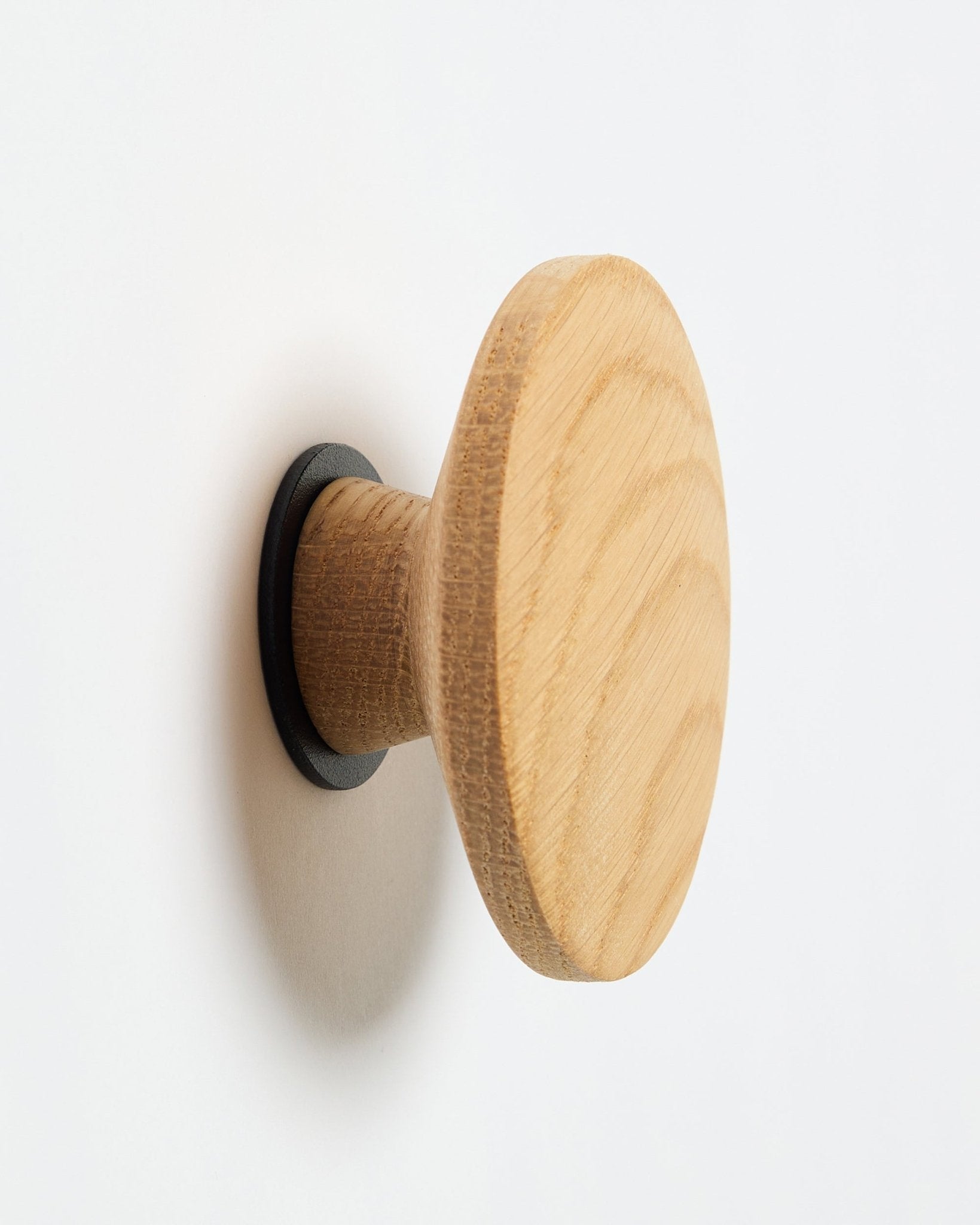 WoodUpp Linn I Single Hanger in natural oak, ein runder Wandhaken mit black Basis, entworfen als Accessoire zur Montage an Akupanel Akustik-Holzpaneelen.