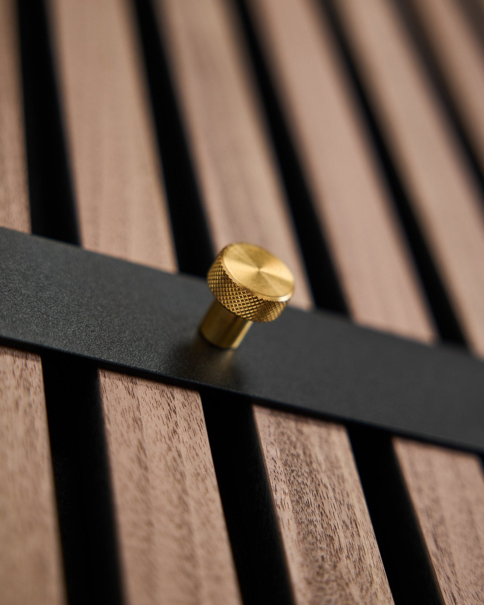 Die WoodUpp Norr Garderobenleiste hat sieben black Haken mit brass Knäufen, montiert auf einem brown Lamellenpaneel, entworfen als nordisches Accessoire für Akupanel.
