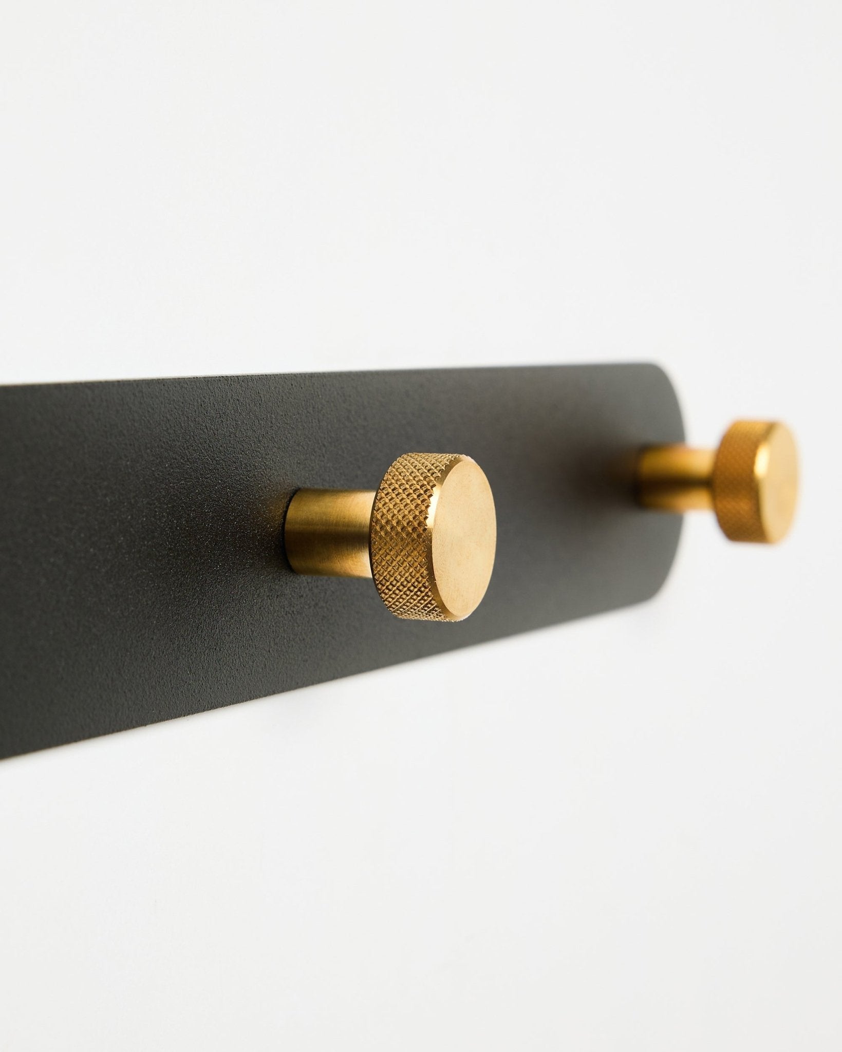 WoodUpp Norr Garderobenleiste, Modell X7, mit zwei zylindrischen black und brass Haken auf einer black Halterung, präsentiert vor weißem Hintergrund.