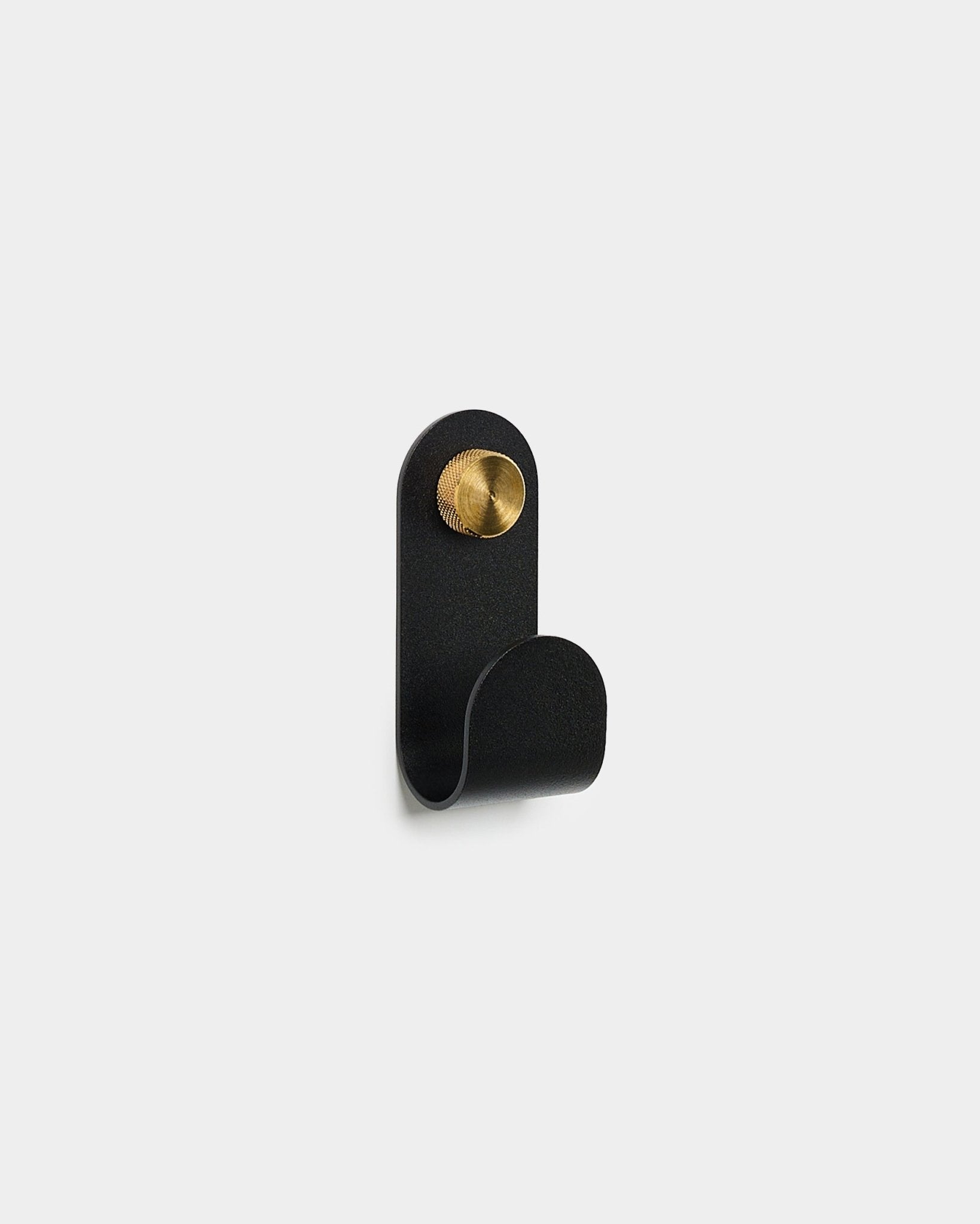 Der Norr Single Hanger in black von WoodUpp, mit gebogenem Design und rundem Akzent in brass, ist vor einem schlichten weißen Hintergrund zu sehen.