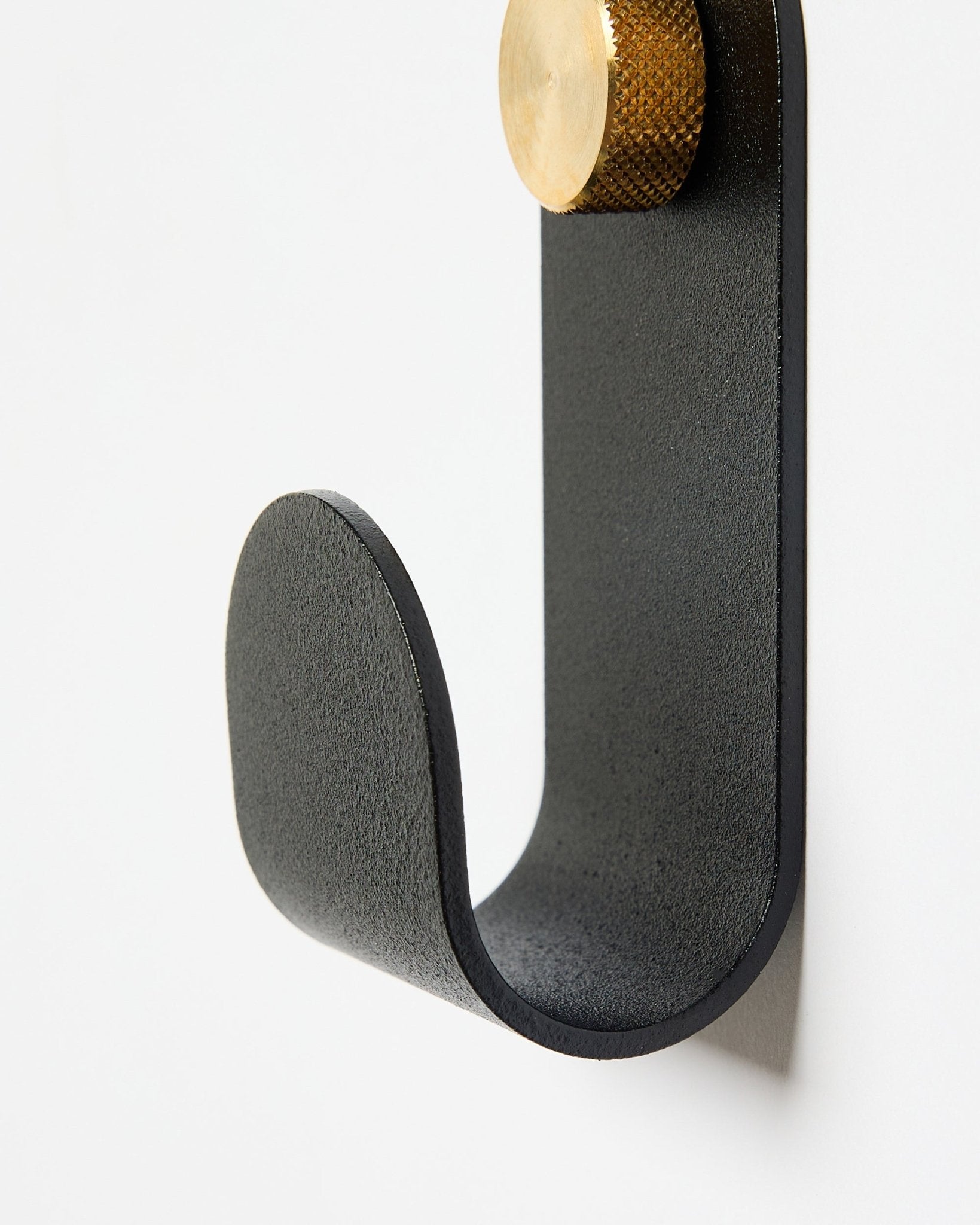 Der Norr Single Hanger von WoodUpp hat einen gebogenen Metallarm in black mit goldfarbener Kappe und ist als Zubehör für die Verwendung mit Akustikpaneelen an weißen Wänden konzipiert.
