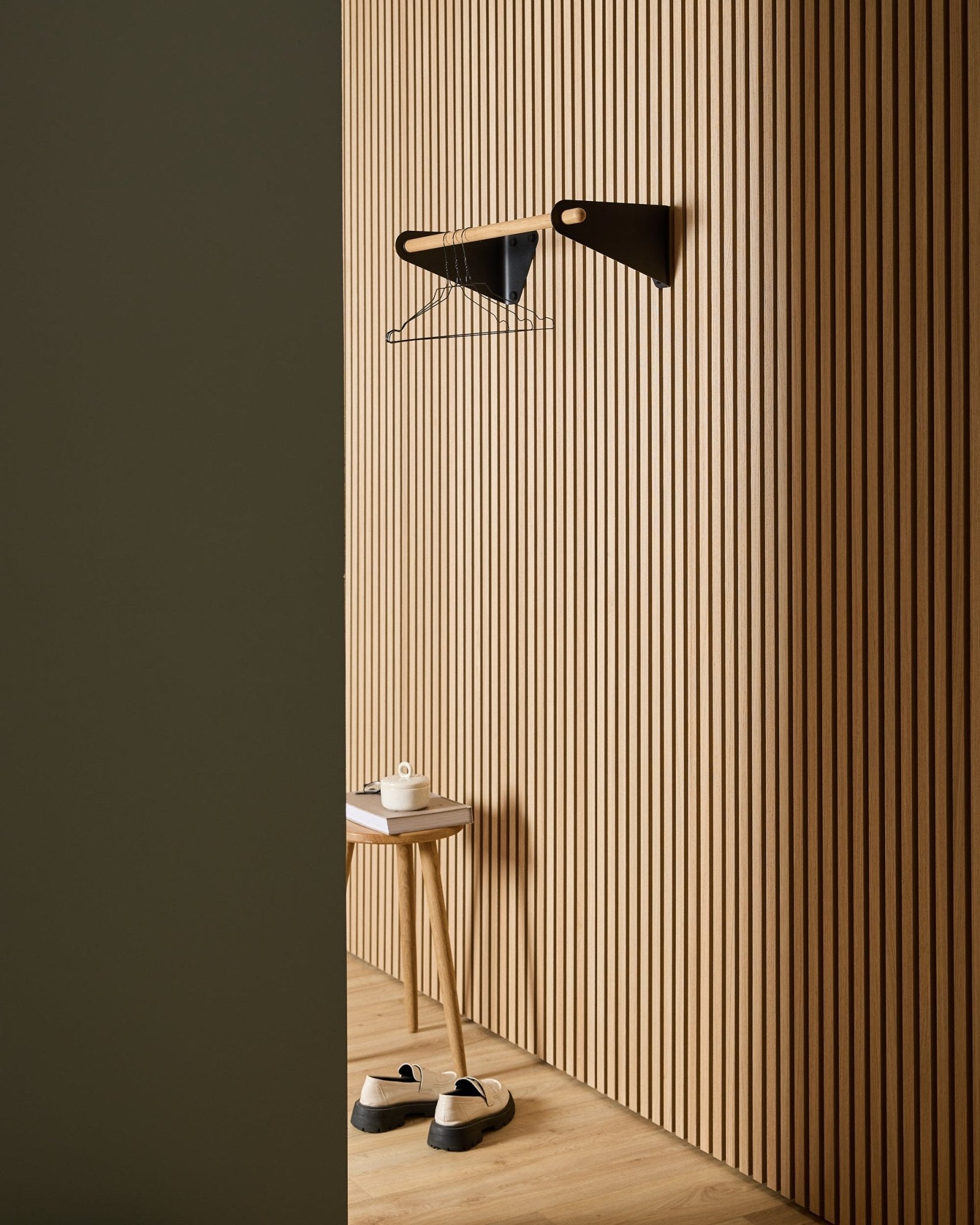 Minimalistischer Eingangsbereich mit WoodUpp Akupanel nordischen Akustik-Holzlamellenpaneelen, black Linn Garderobenleiste (75,9 cm), Hocker, Schuhen, Wandregal und Papierrolle.