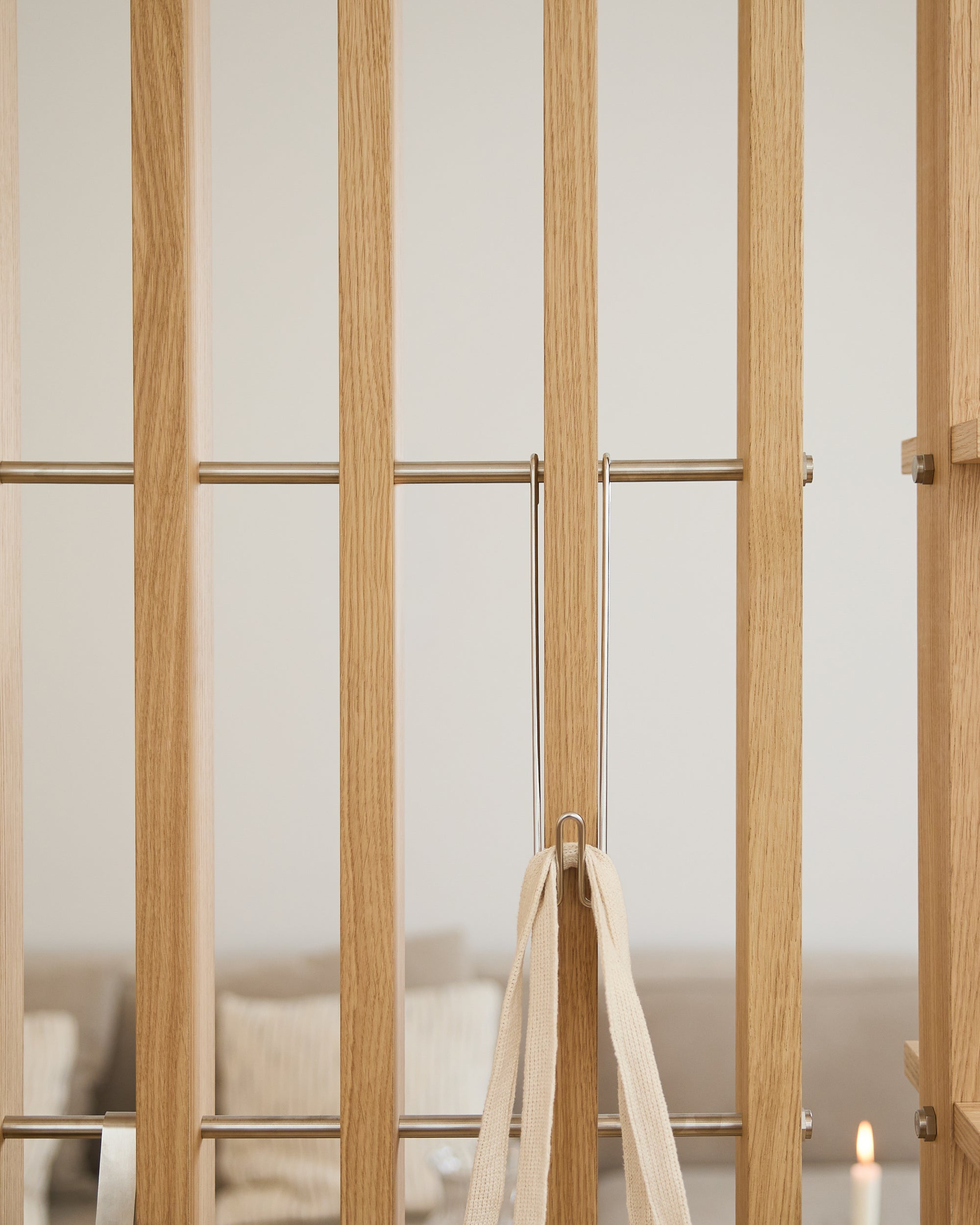 Helles Holztor mit Metallstangen, beiger Schleife und drei WoodUpp Alva Wire Hooks/BM1; im Hintergrund ein unscharfes Sofa und eine Kerze.