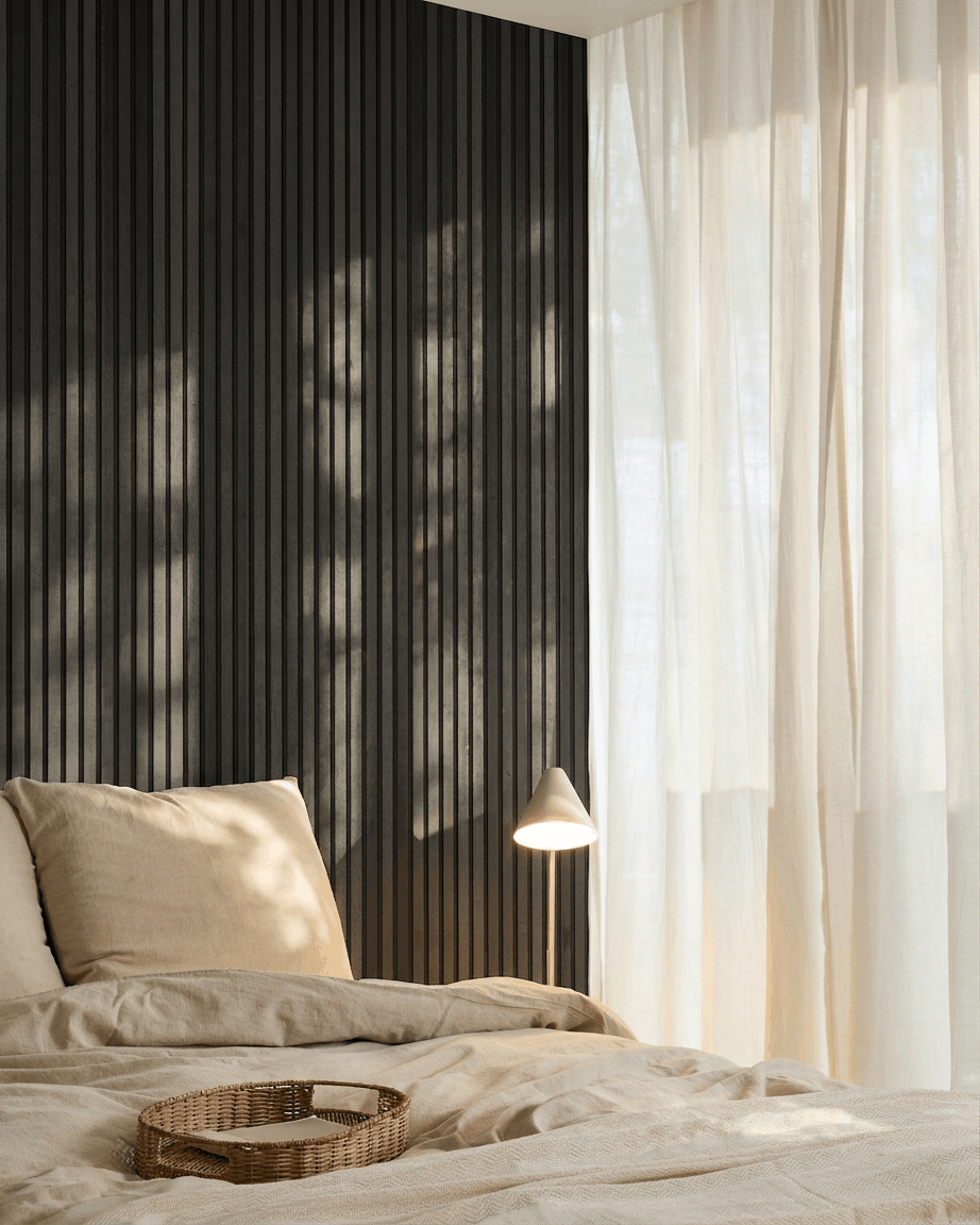 Minimalistisches nordisches Schlafzimmer mit einem WoodUpp Akupanel Akustikpaneel in Black Ash, beige Bettwäsche, einem Tablett aus Rattan und transparenten Vorhängen, die natürliches Licht hereinlassen.