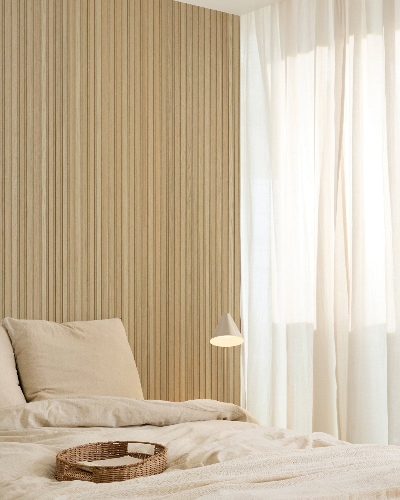 Minimalistisches Schlafzimmer mit beige Bettwäsche, einem Tablett aus Rattan, moderner Wandleuchte, einer Akupanel Akustikholzpaneel-Akzentwand und transparenten Vorhängen, die weiches natürliches Licht filtern.
