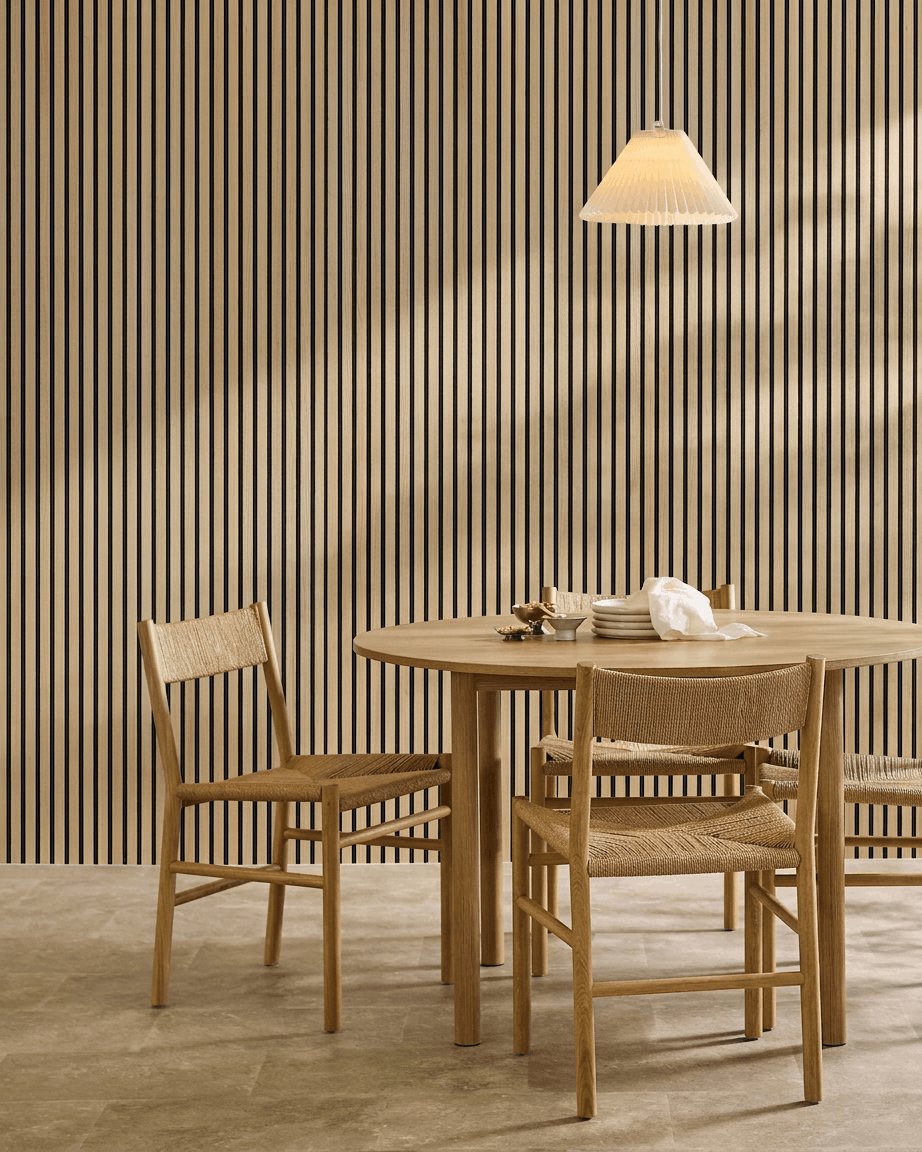 Minimalistischer Essbereich mit rundem Tisch, geflochtenen Stühlen, Pendelleuchte und einem an der Wand montierten WoodUpp Akupanel Classic Oak Akustikpaneel.