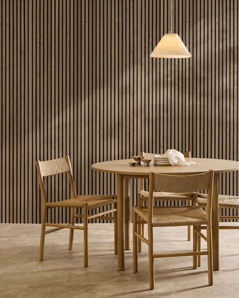 Minimalistischer Essbereich mit rundem Tisch, geflochtenen Stühlen, Pendelleuchte und einem akustischen Holzpaneel WoodUpp Akupanel in Natural Wood mit black Filz an der Wand.