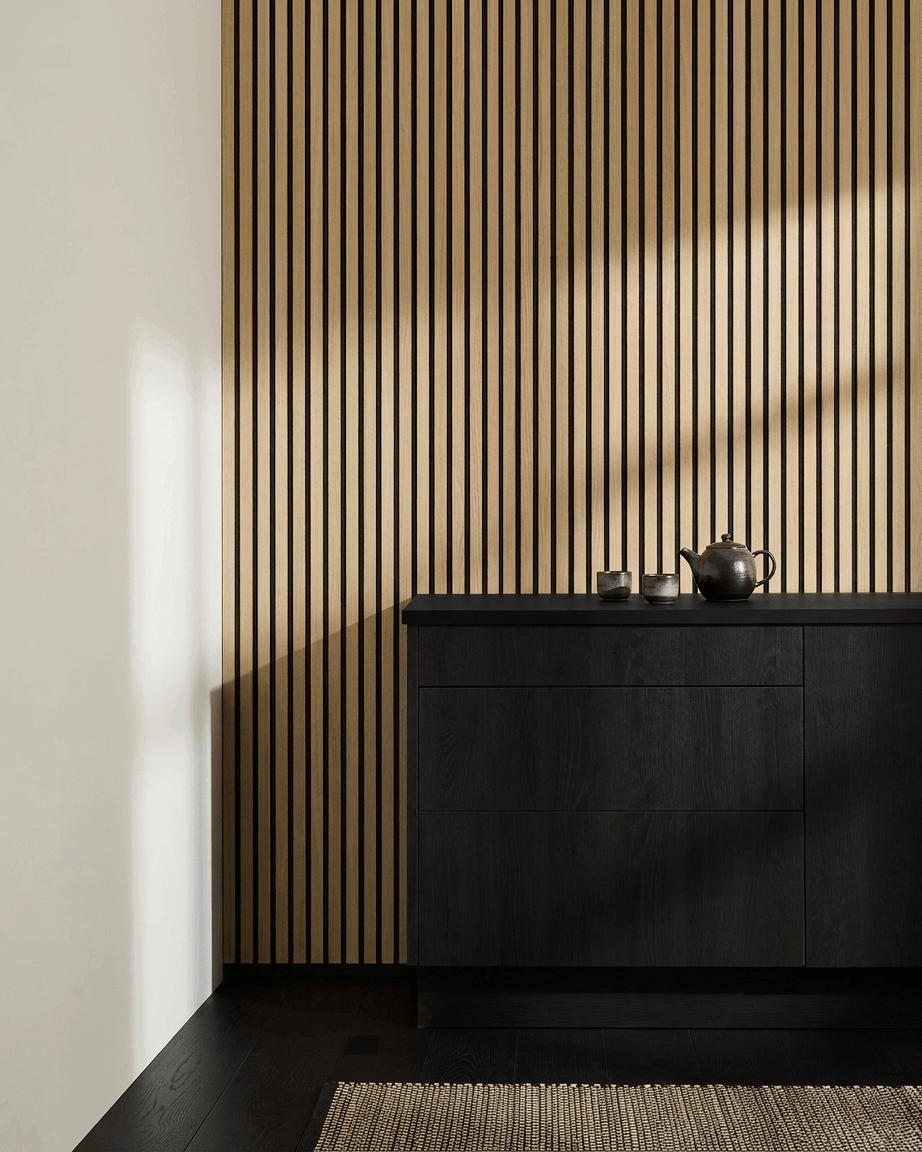 Minimalistische nordische Küche mit WoodUpp Akupanel Akustikpaneel in Classic Oak, black Schrank, Teekanne, Tassen und gewebtem Teppich auf dunklem Holzboden.