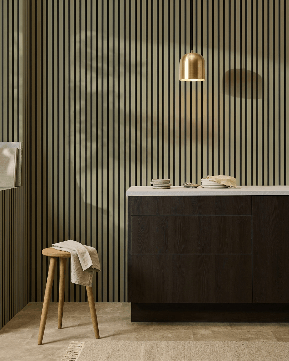 Moderne Küche mit dunklen Holzschränken, Marmorarbeitsplatte, brass Pendelleuchte und einem WoodUpp Akupanel Colored Akustik-Lamellenwandpaneel zur Schallabsorption.
