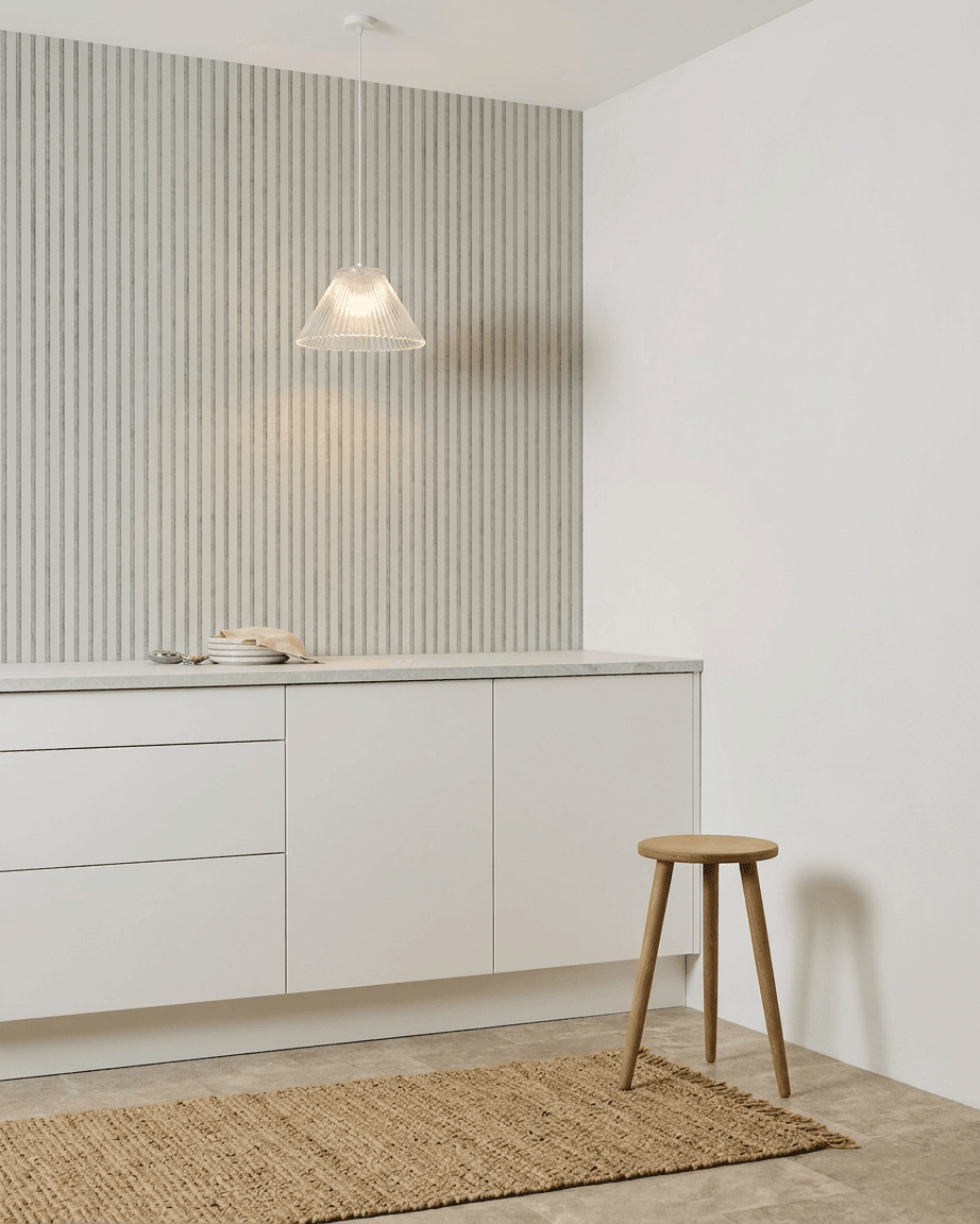 Minimalistische Küche mit weißen Schränken, Holzstuhl, gewebtem Teppich und einem installierten WoodUpp Akupanel Snow Akustikpaneel zur Schallabsorption.