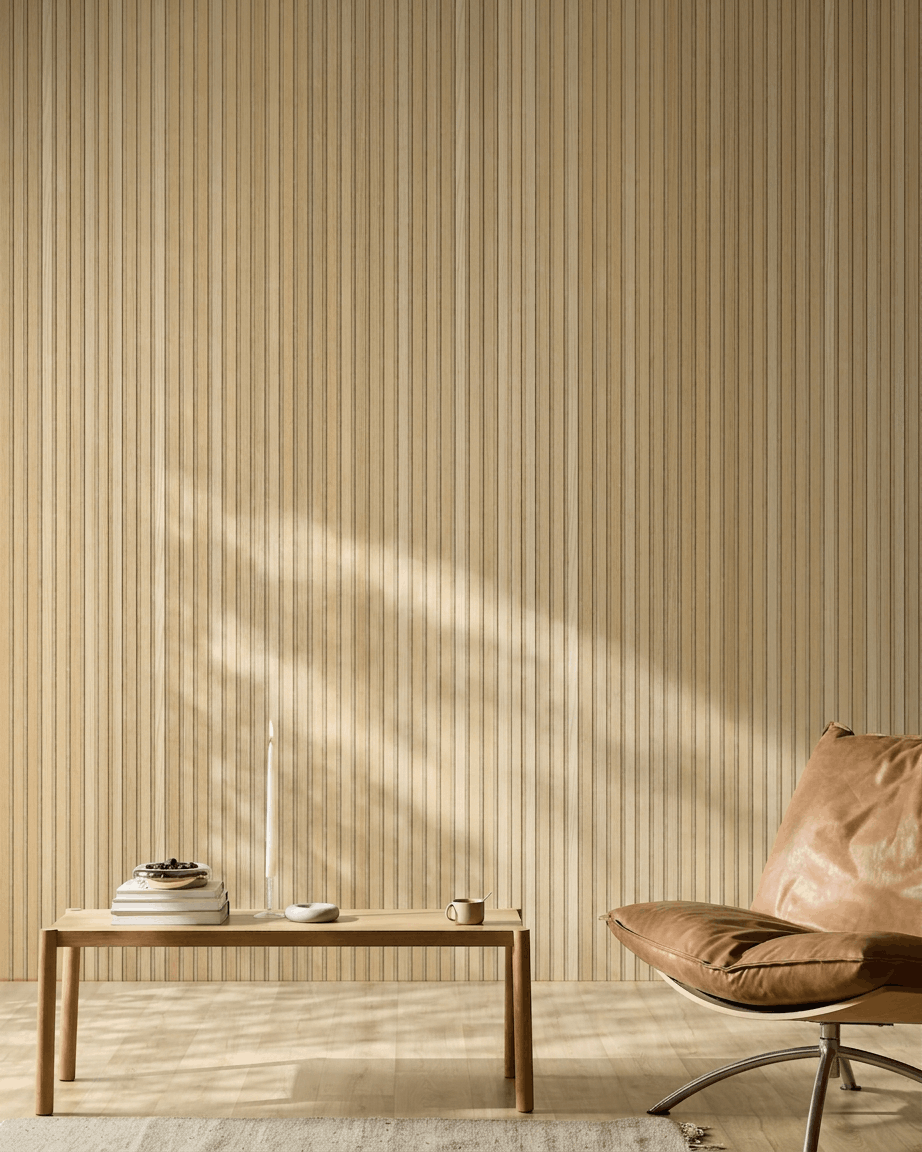 Minimalistischer skandinavischer Raum mit einem WoodUpp Akupanel Akustikholzpaneel in Natural Wood Classic Oak, einem Sessel aus hellbraunem Leder und einem schlichten Holztisch mit wohnlichen Akzenten.
