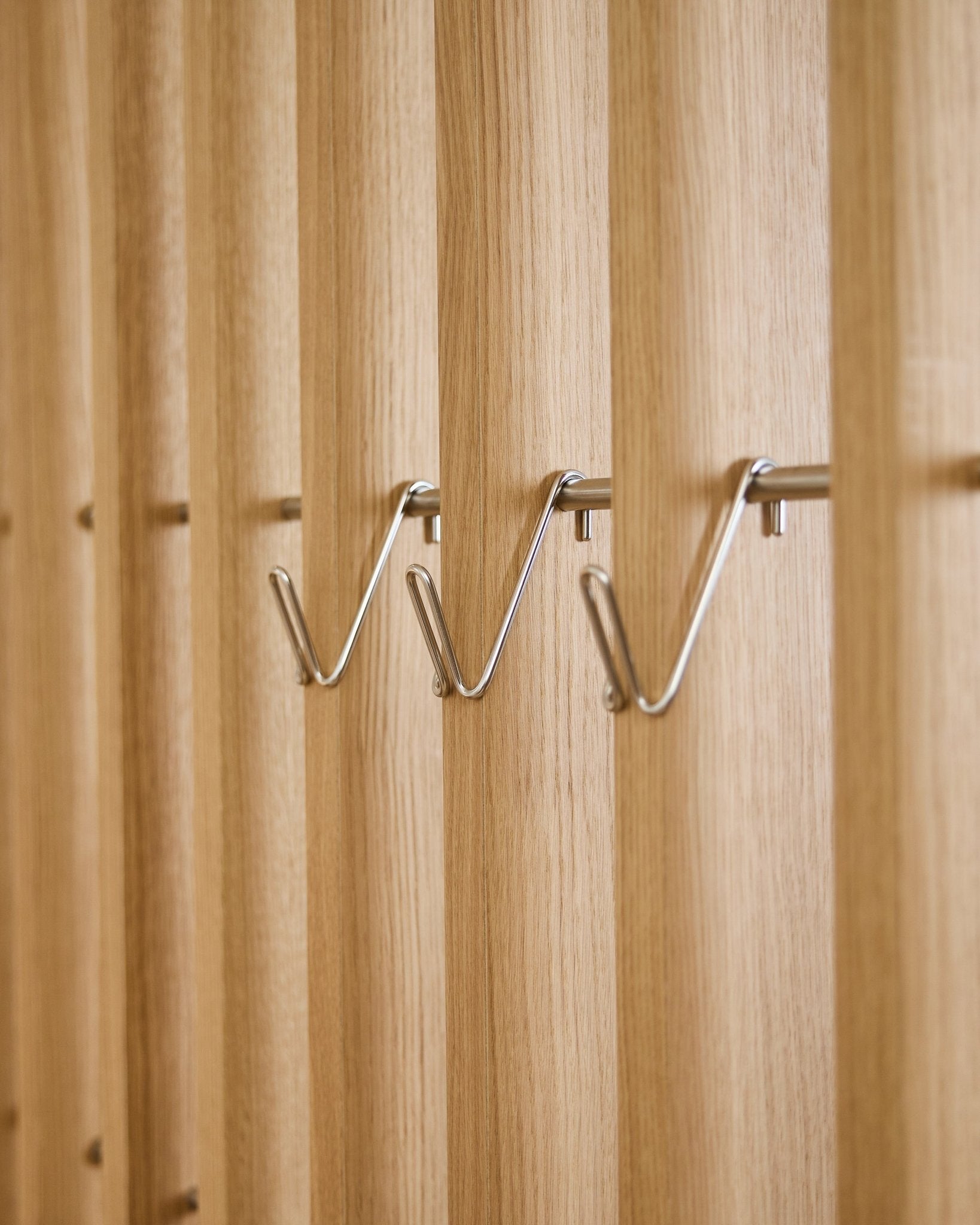 Drei kurze Alva Wire Hook / BM1 Accessoires von WoodUpp aus Edelstahl steel sind gleichmäßig in einer Reihe auf einem Akustik-Holzlamellenpaneel vertical montiert.