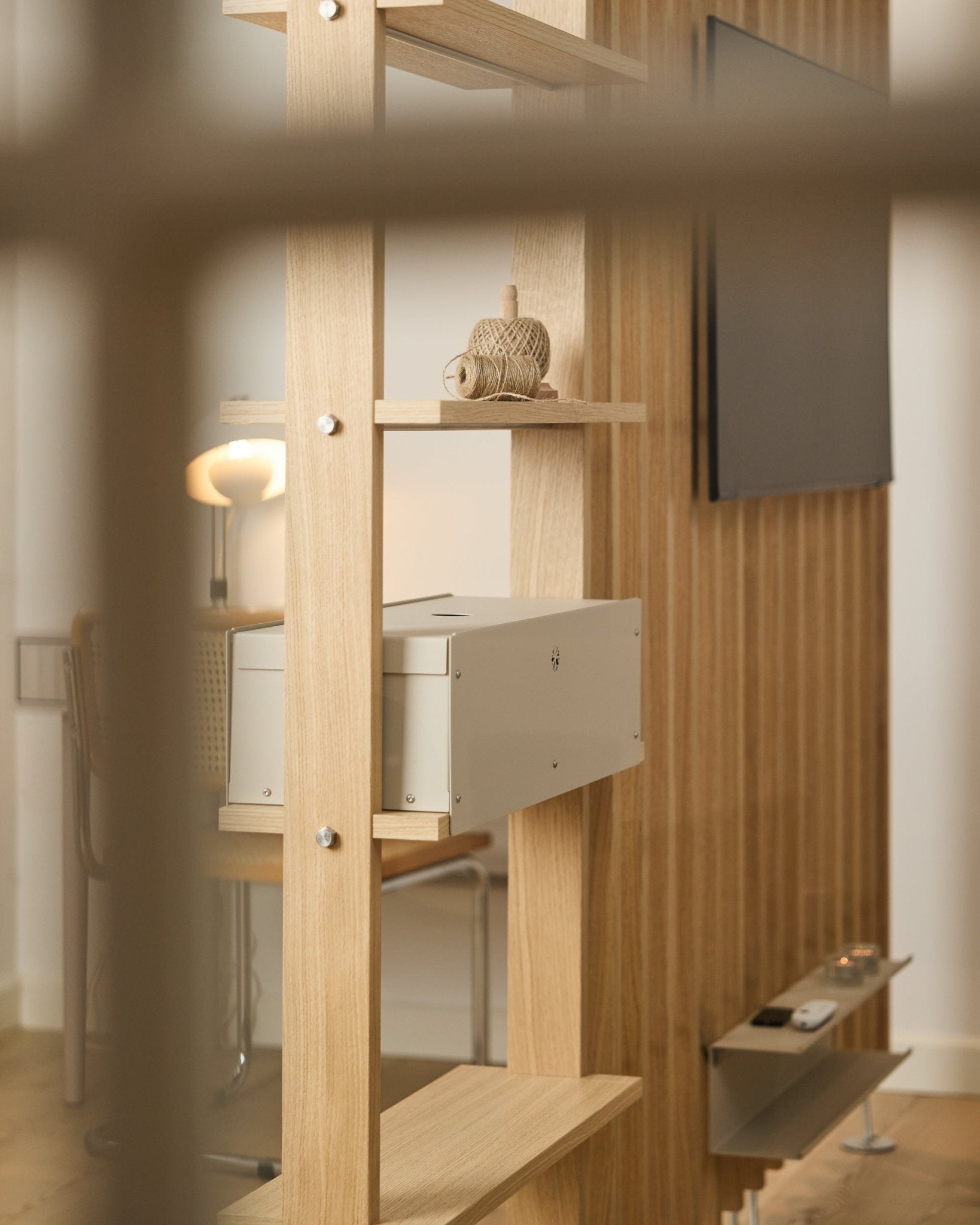 Ein gemütlicher Raum mit Stuhl, Lampe und Fernseher zeigt das Nell | Metal Box / BM2 Regal von WoodUpp in beige, ergänzt durch eine minimalistische nordische Einrichtung.