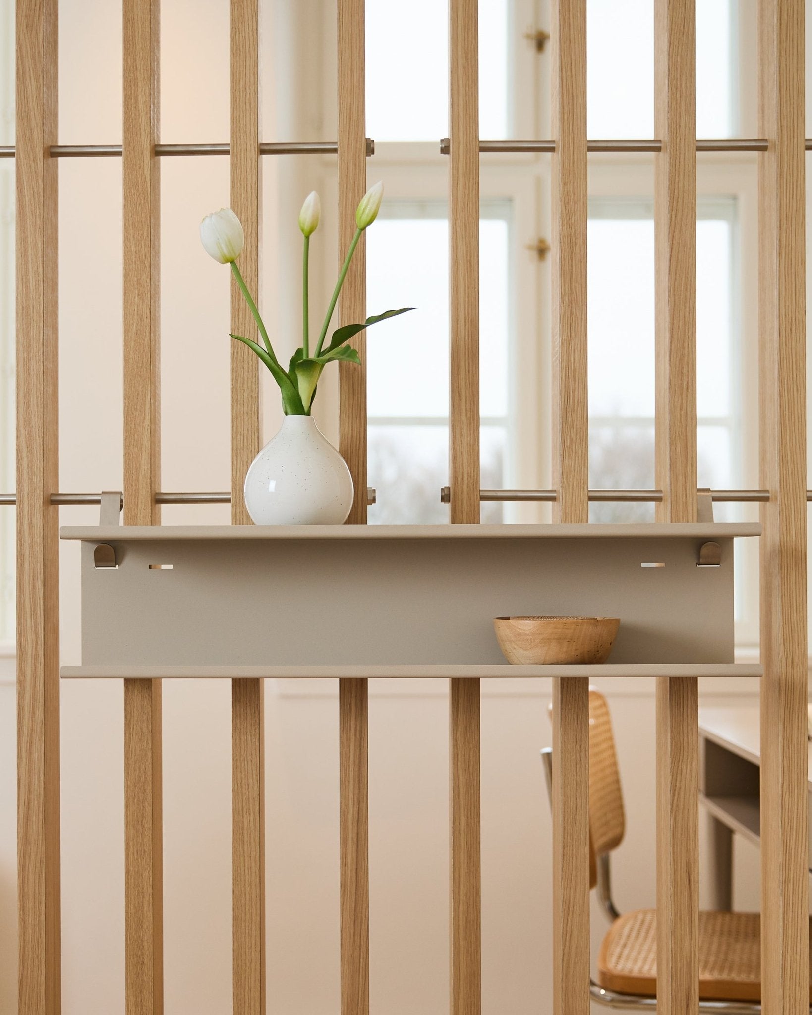 Double Metal Shelf / BM1 von WoodUpp in beige (63,5 cm), montiert an einem Lamellen-Raumteiler und dekoriert mit einer Vase und einer Holzschale.