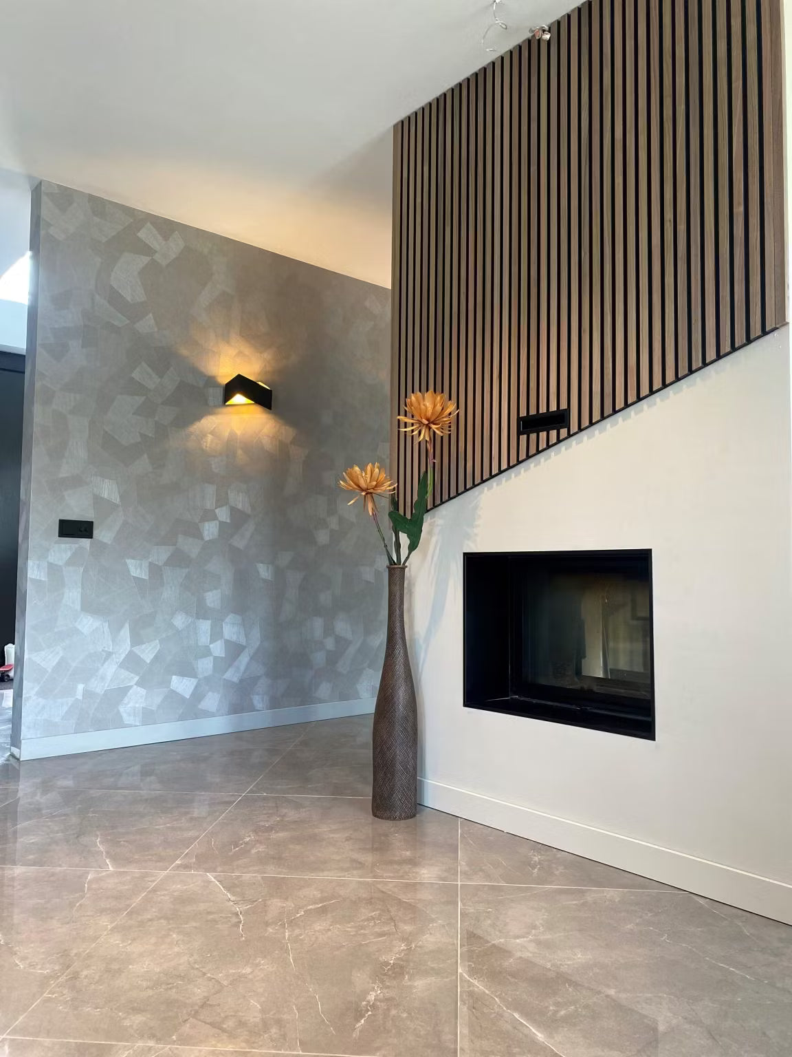 Modernes Wohnzimmer mit geometrisch gemusterter Tapete, Akupanel-Holzakustikverkleidung, Wandkamin und einer hohen Vase mit orangefarbenen Blumen.